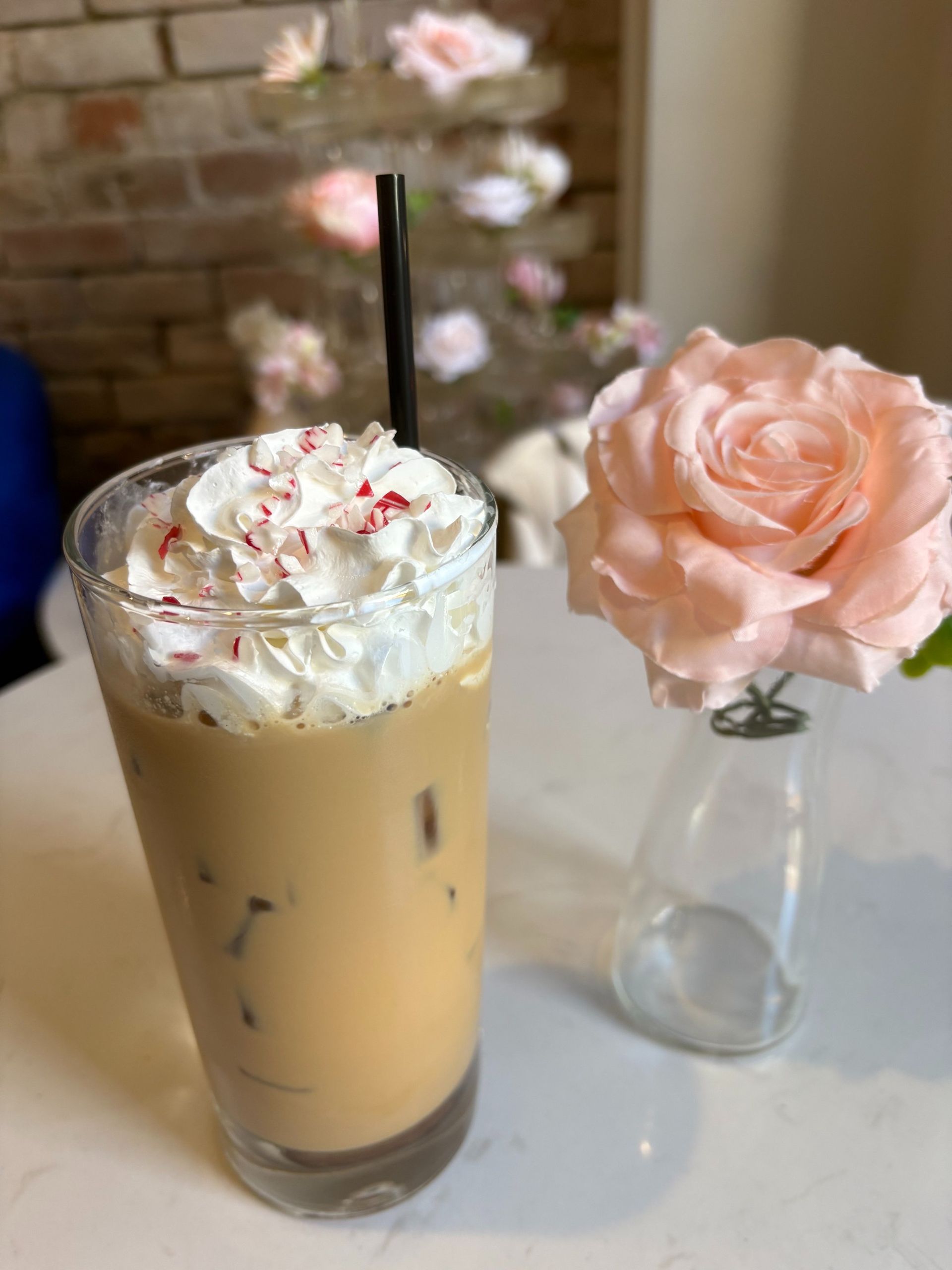 Iced coffee drink with whipped cream and a pink rose on a white table.