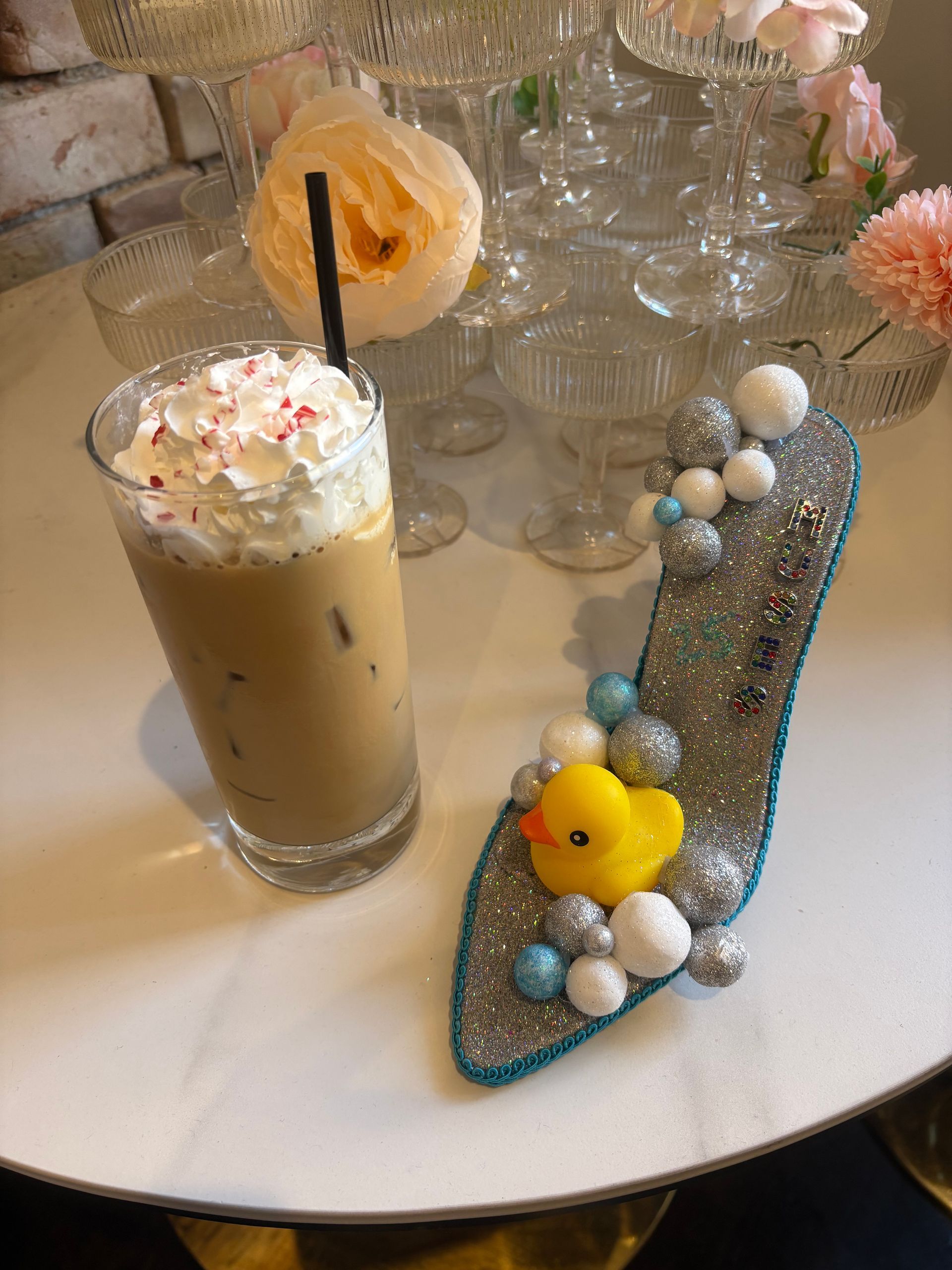 Iced coffee with whipped cream and a decorated shoe with a rubber duck on a table.