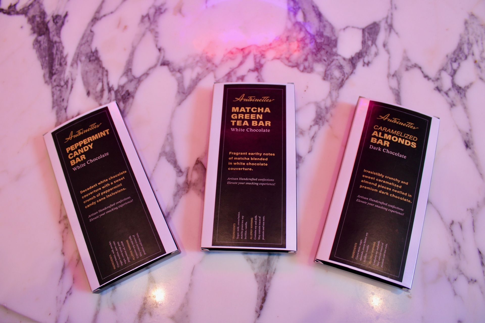Three chocolate bars in black and white packaging on a marble surface. The center bar is labeled 