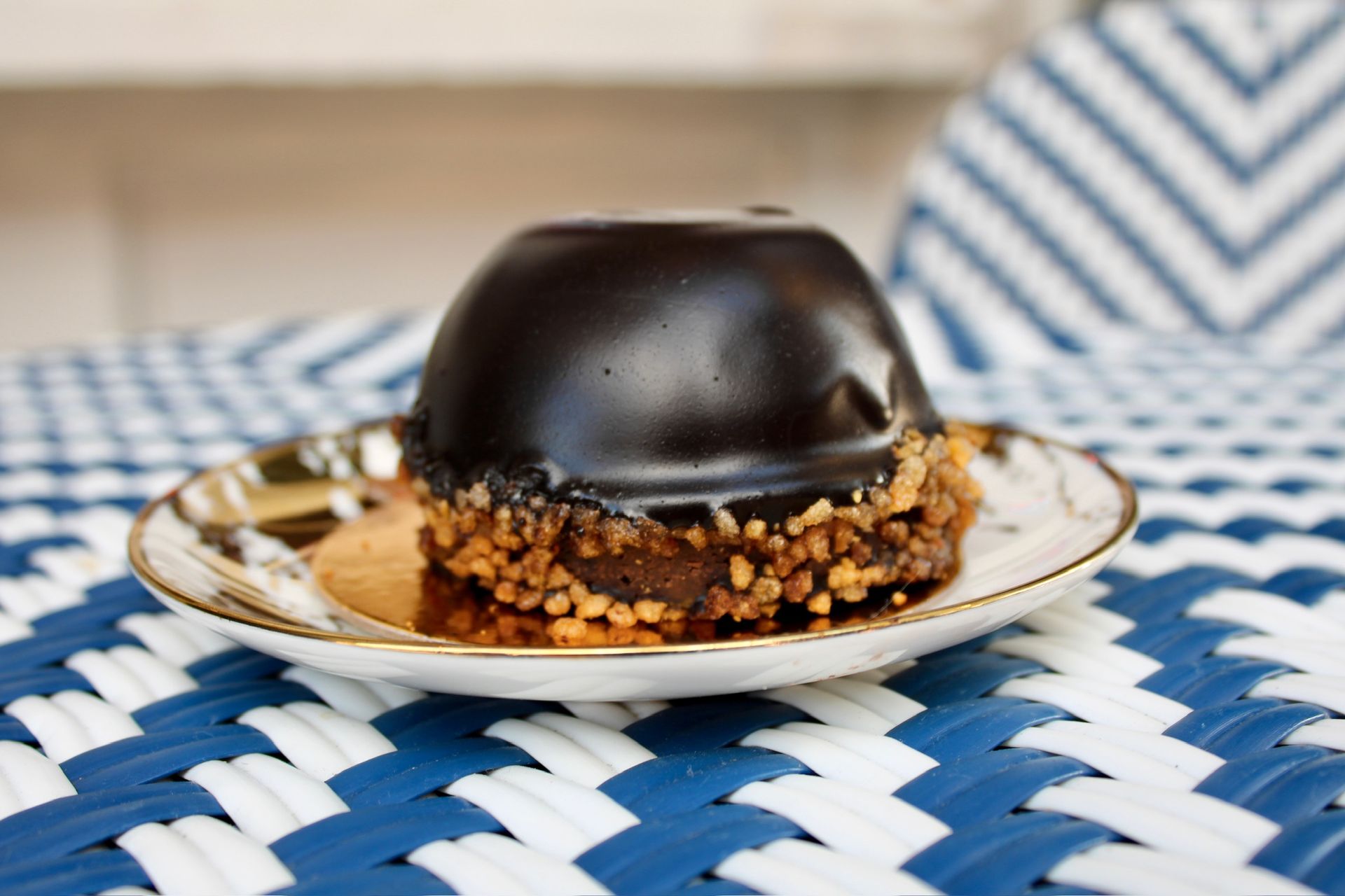 Chocolate-covered cake with chopped nuts on a small plate with a blue and white woven background.