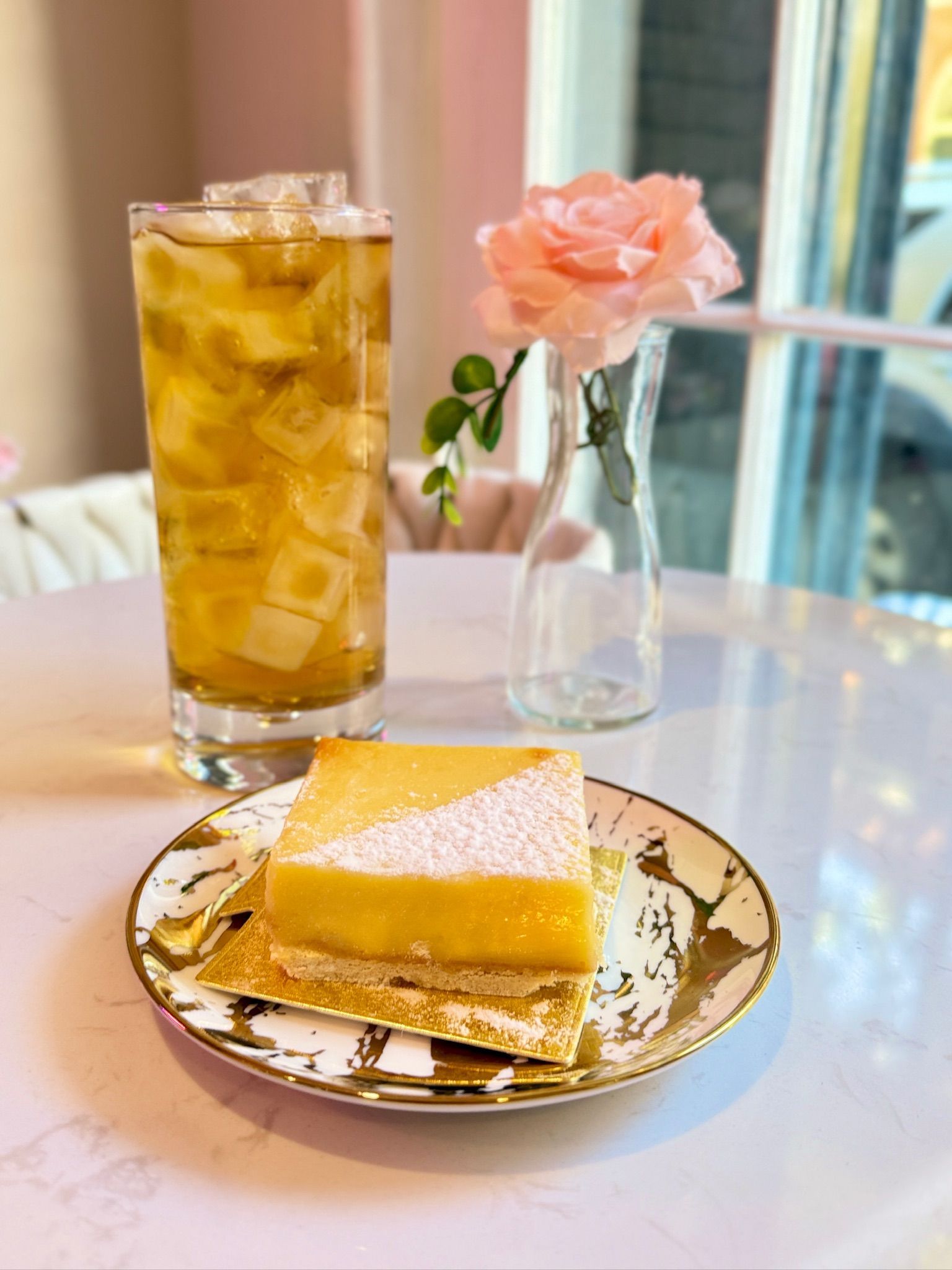 Iced drink, lemon bar, and rose in a vase on a table.