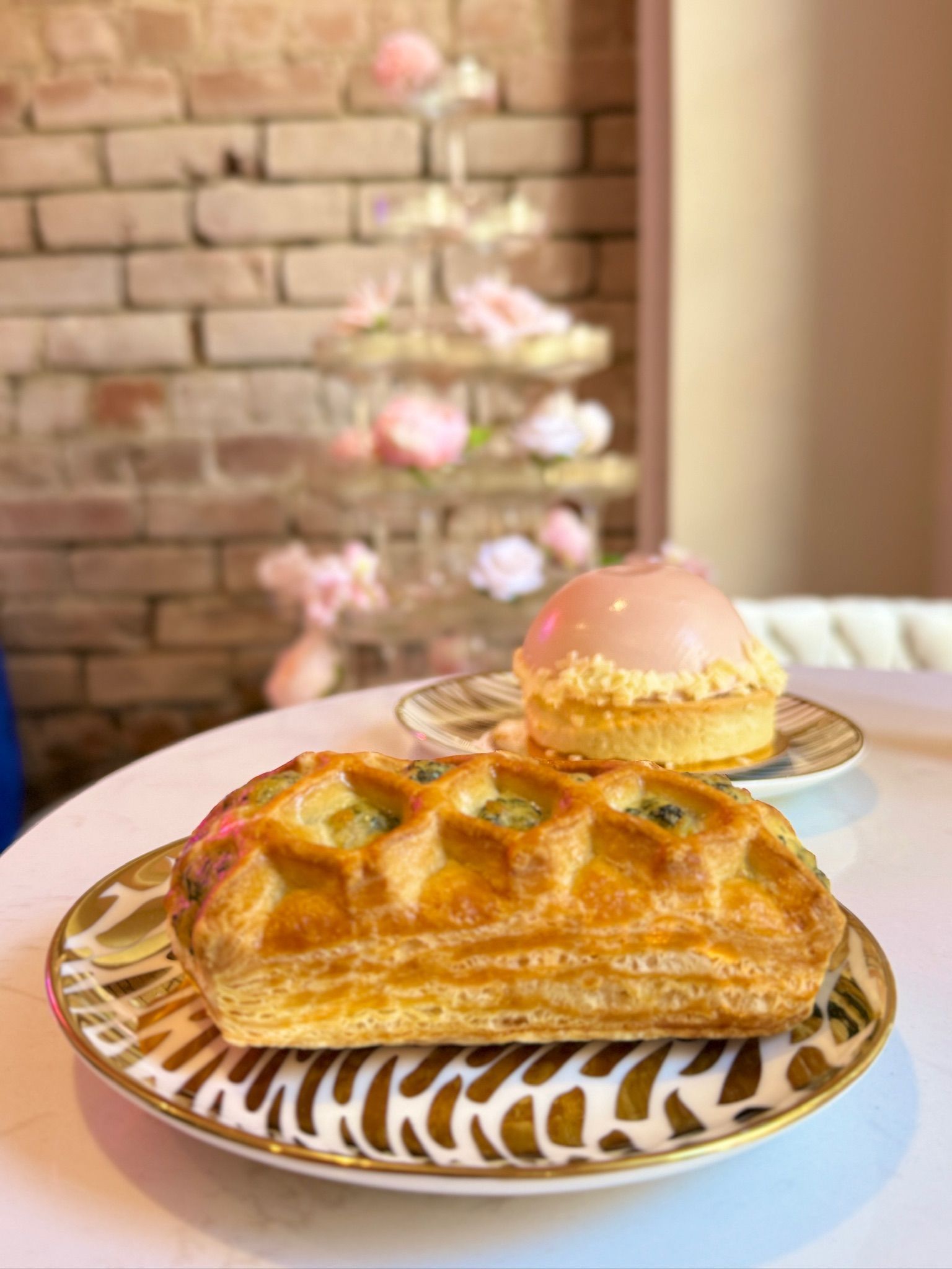 Pastries on plates, one rectangular with green filling, one round with pink glaze, near tiered flower display.