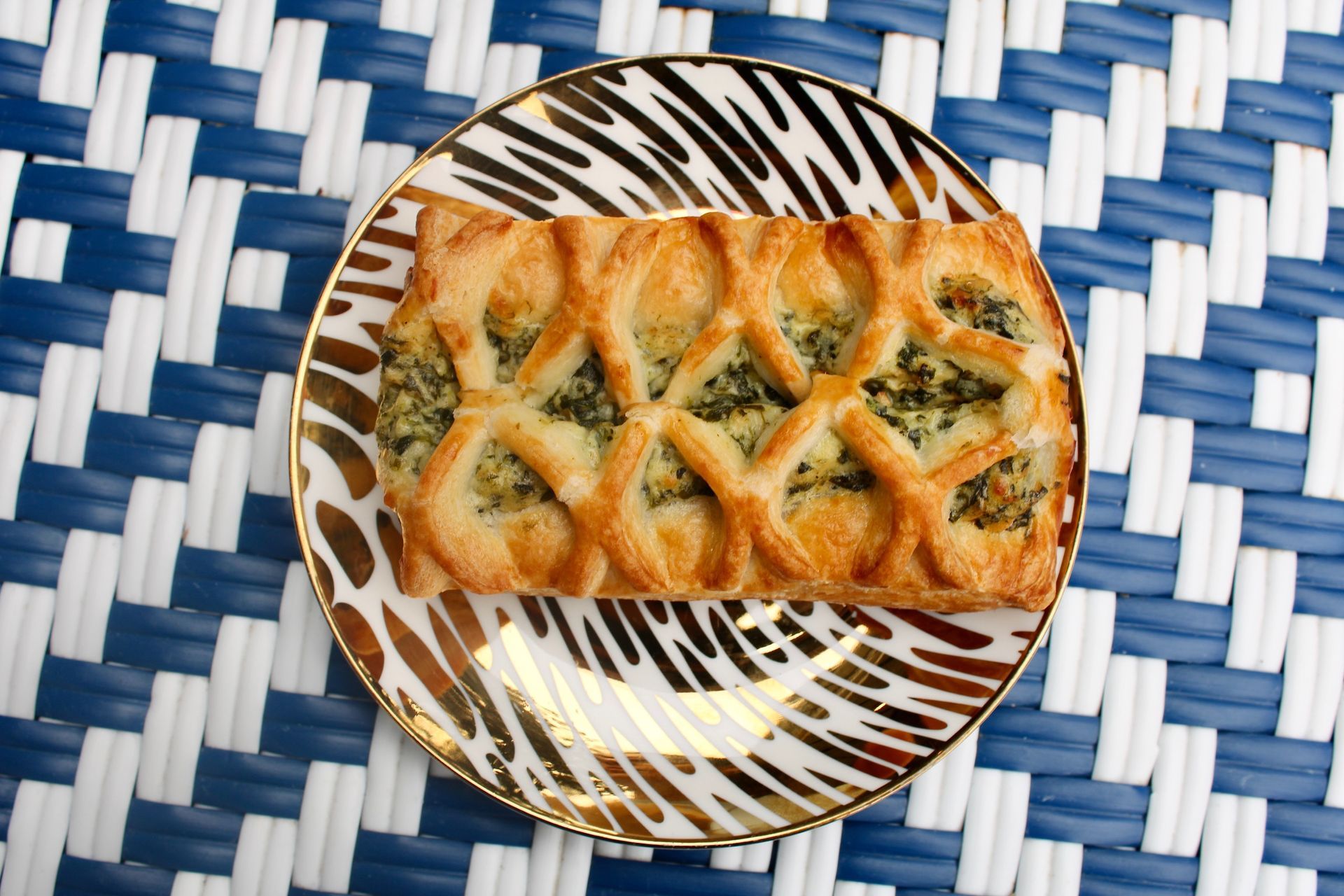 Spinach pastry on a decorative plate, set against a blue and white patterned surface.