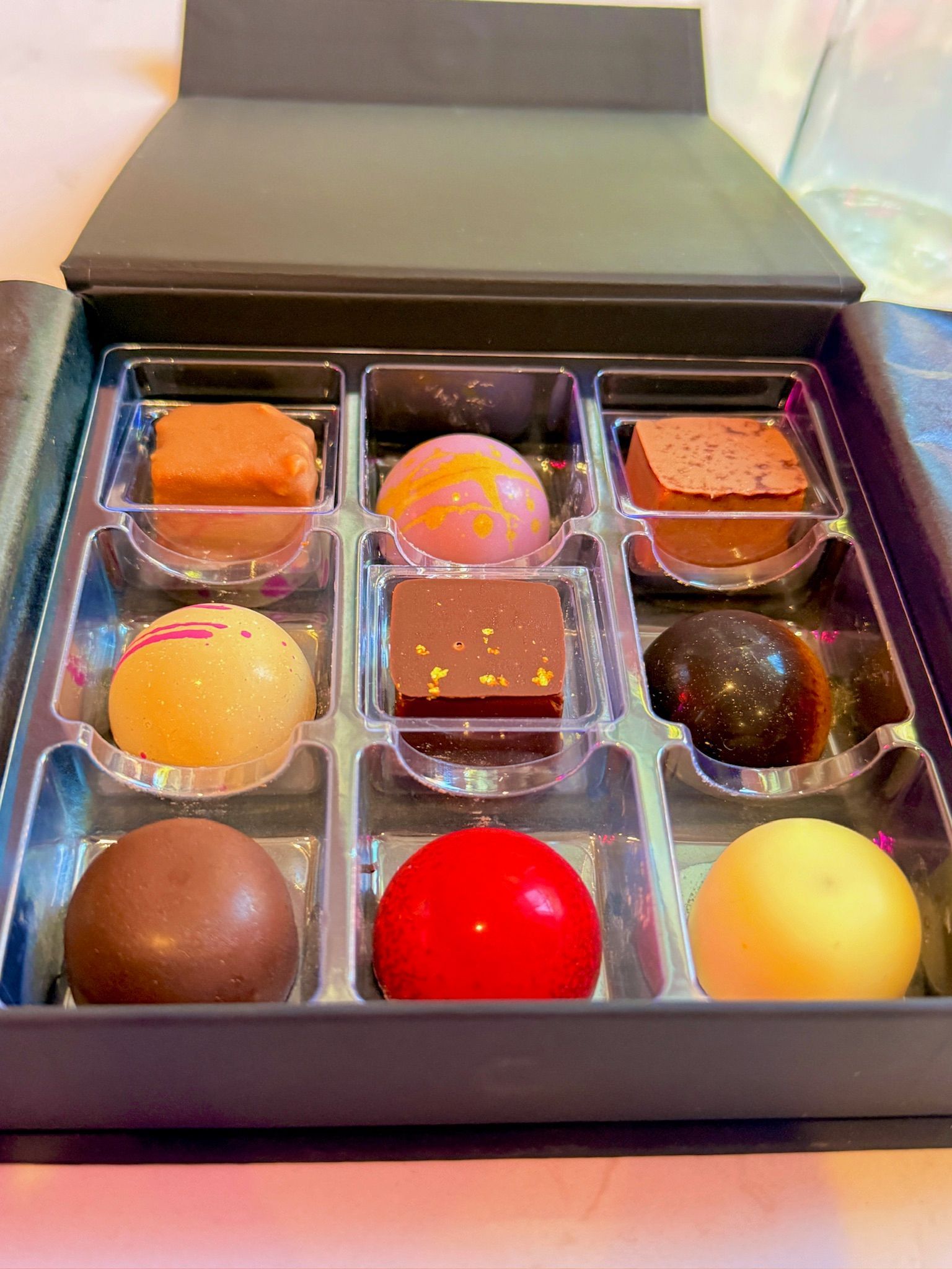 Box of nine assorted chocolates in different colors and shapes.