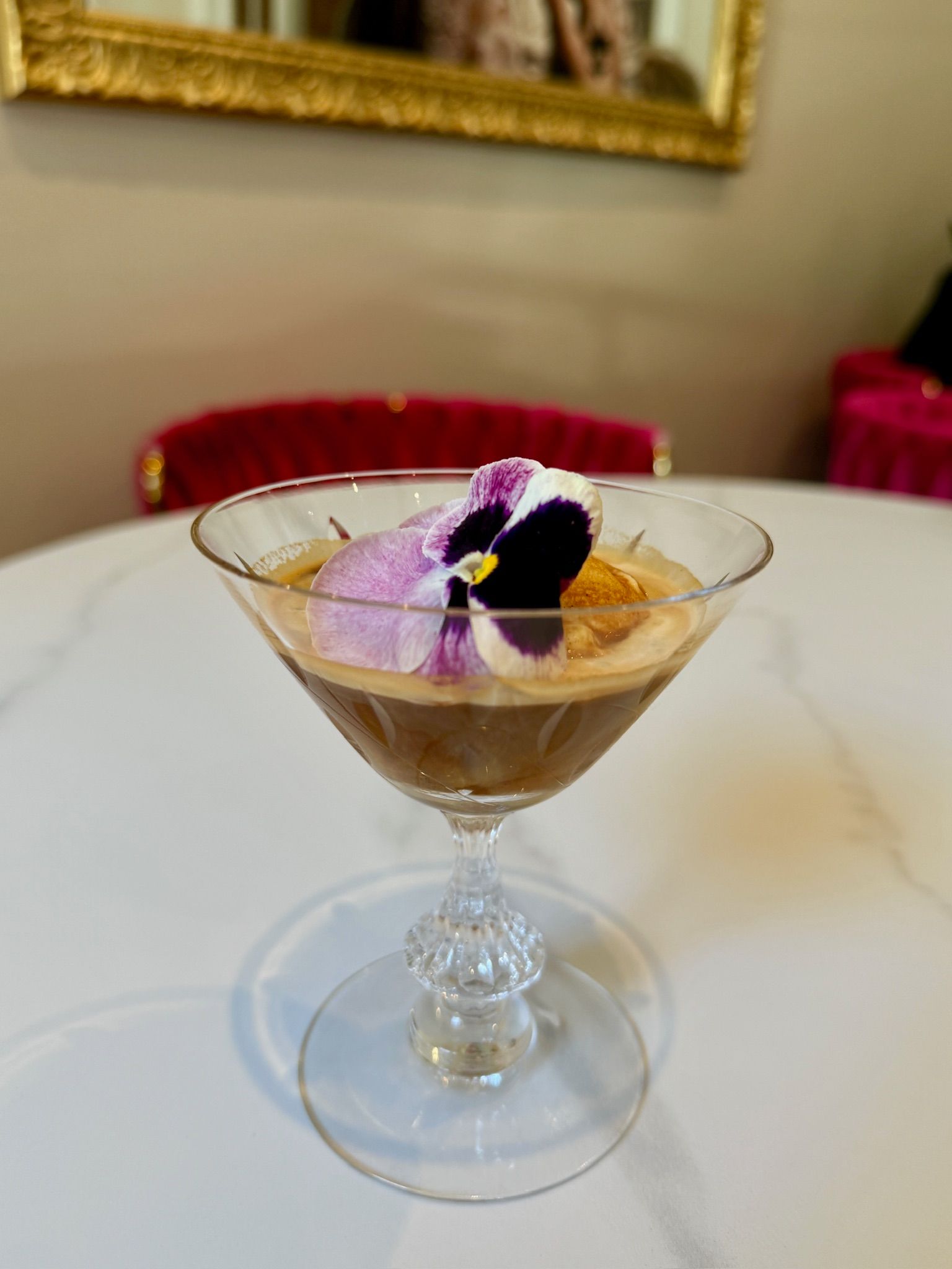 Espresso martini in a crystal glass, garnished with lavender foam and a violet, on a white table.