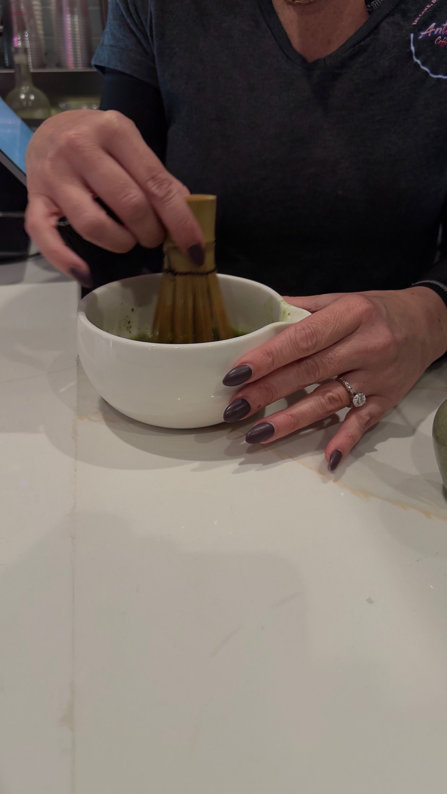 Person whisking matcha tea in a white bowl with a bamboo whisk, close up.