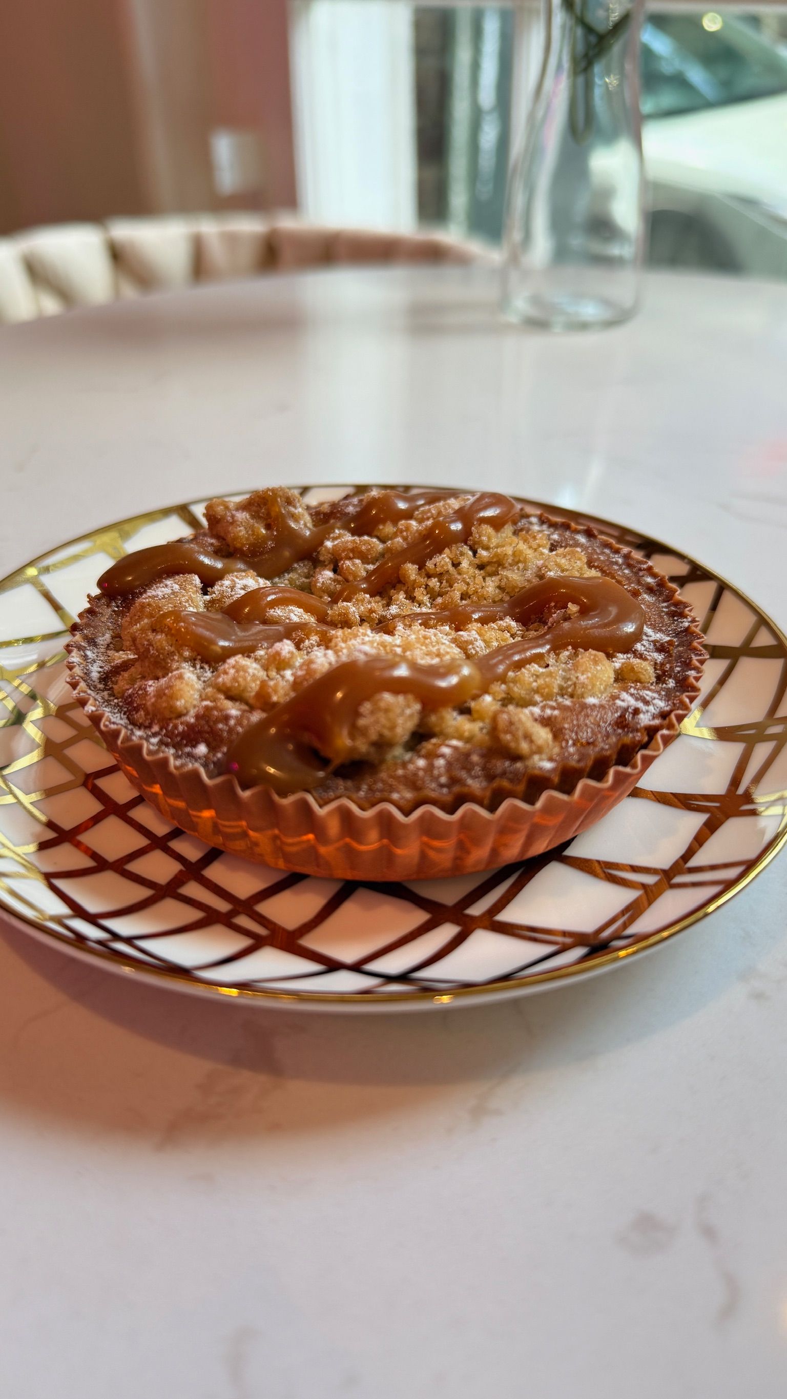 Caramel apple tart on a decorative white and gold plate, on a light marble surface.