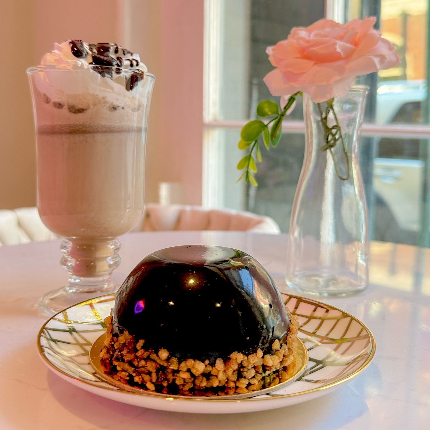Chocolate dessert and coffee drink on a table with a flower in a vase.