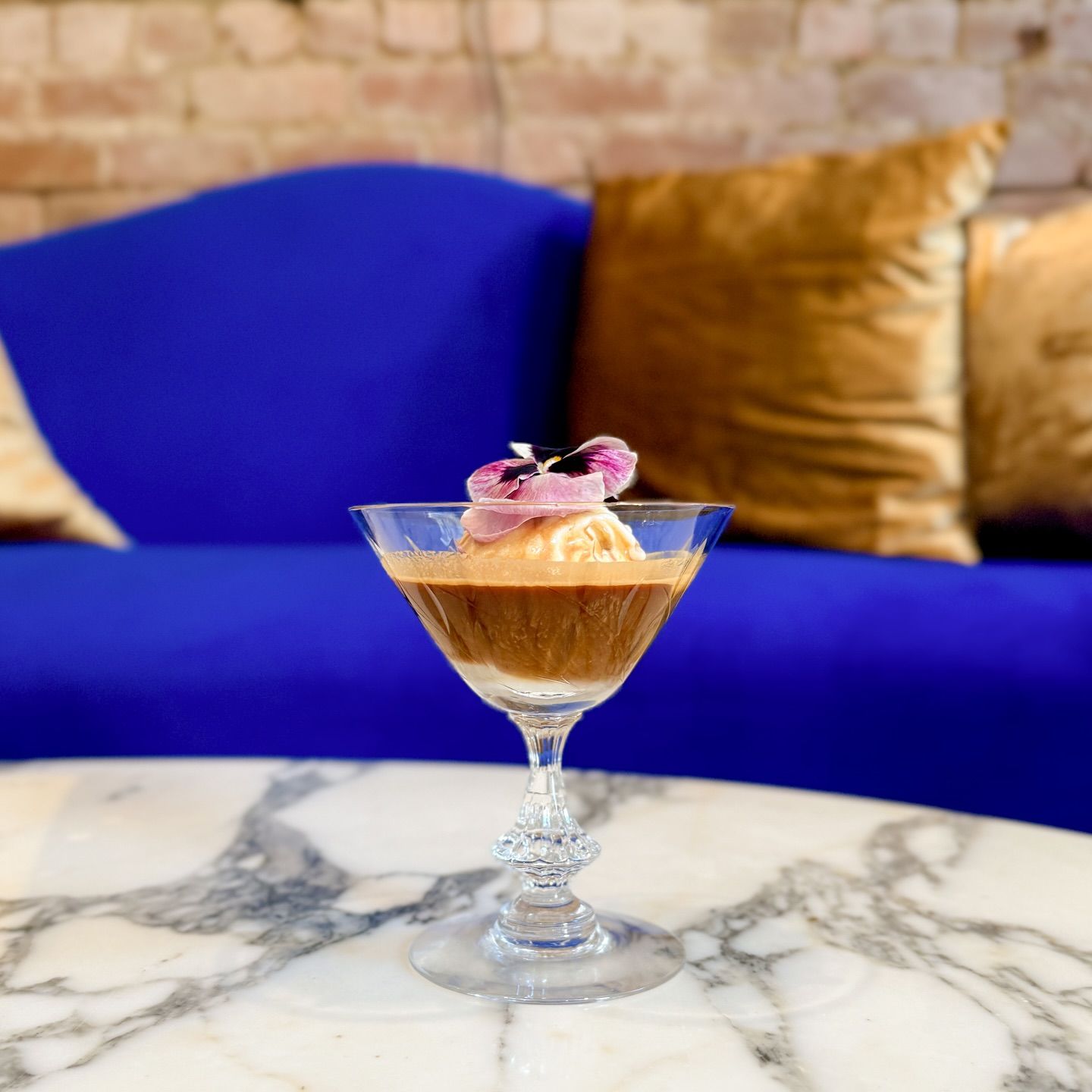 Affogato dessert in a crystal glass, topped with ice cream and a flower, set on a marble table.