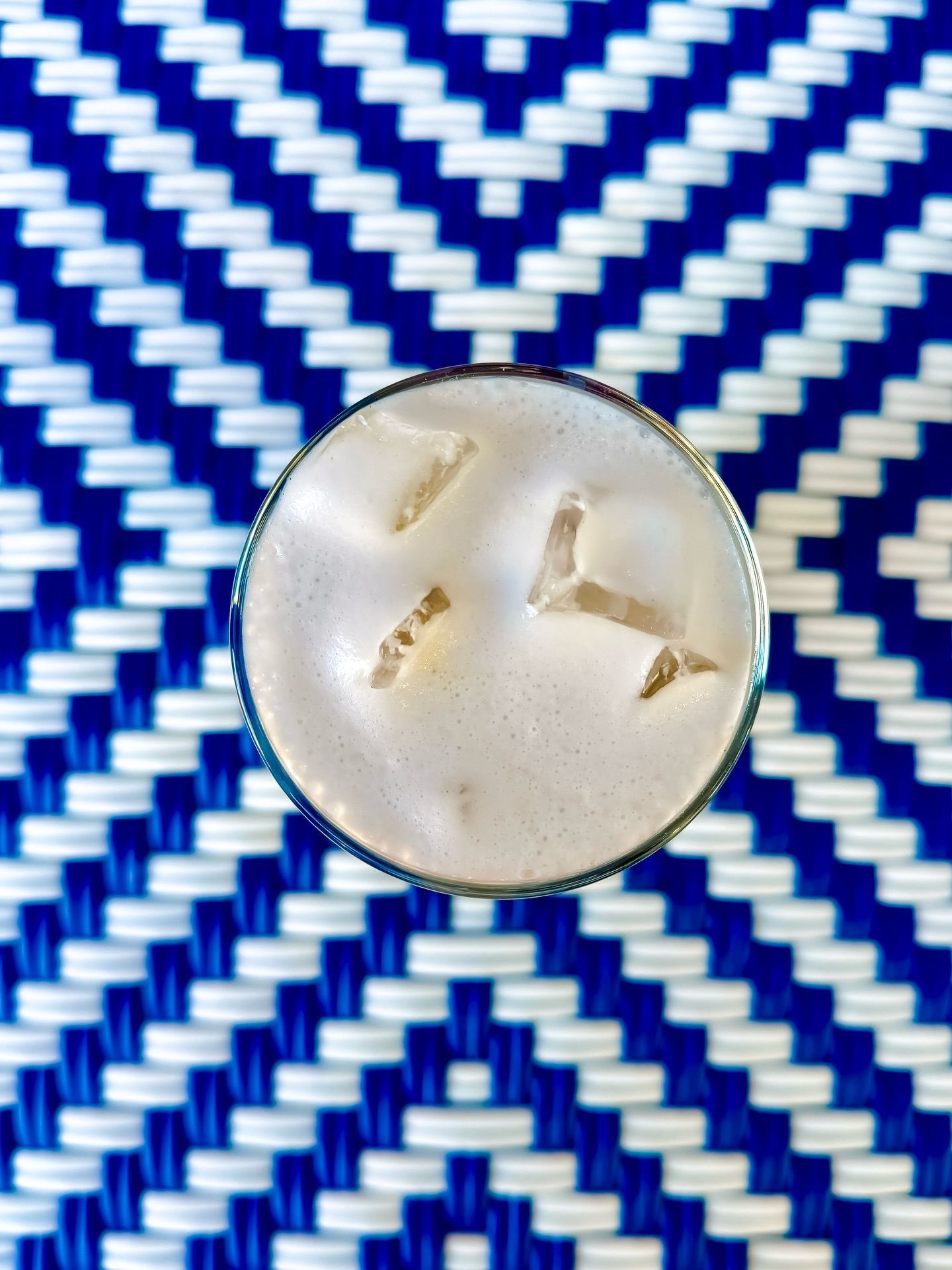 Cocktail in a glass, with ice, on a blue and white patterned surface.