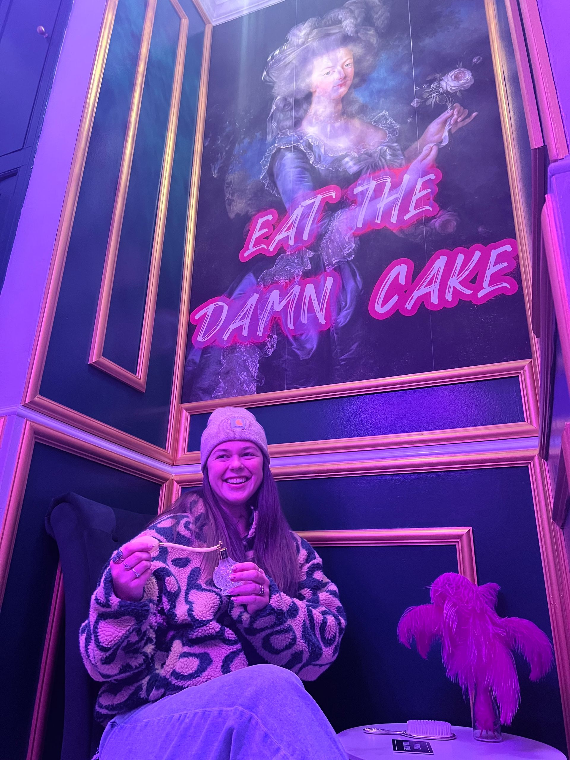 Woman in beanie smiles, seated, holding food in room with 