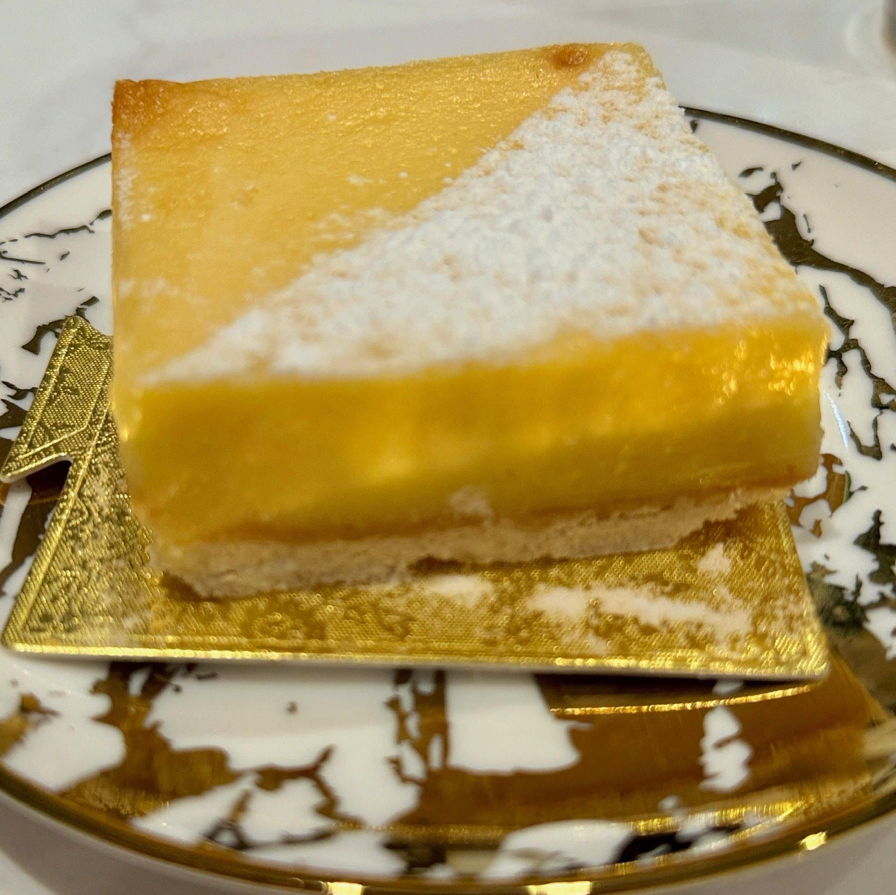 Lemon square dessert on a gold square plate atop a decorative plate.