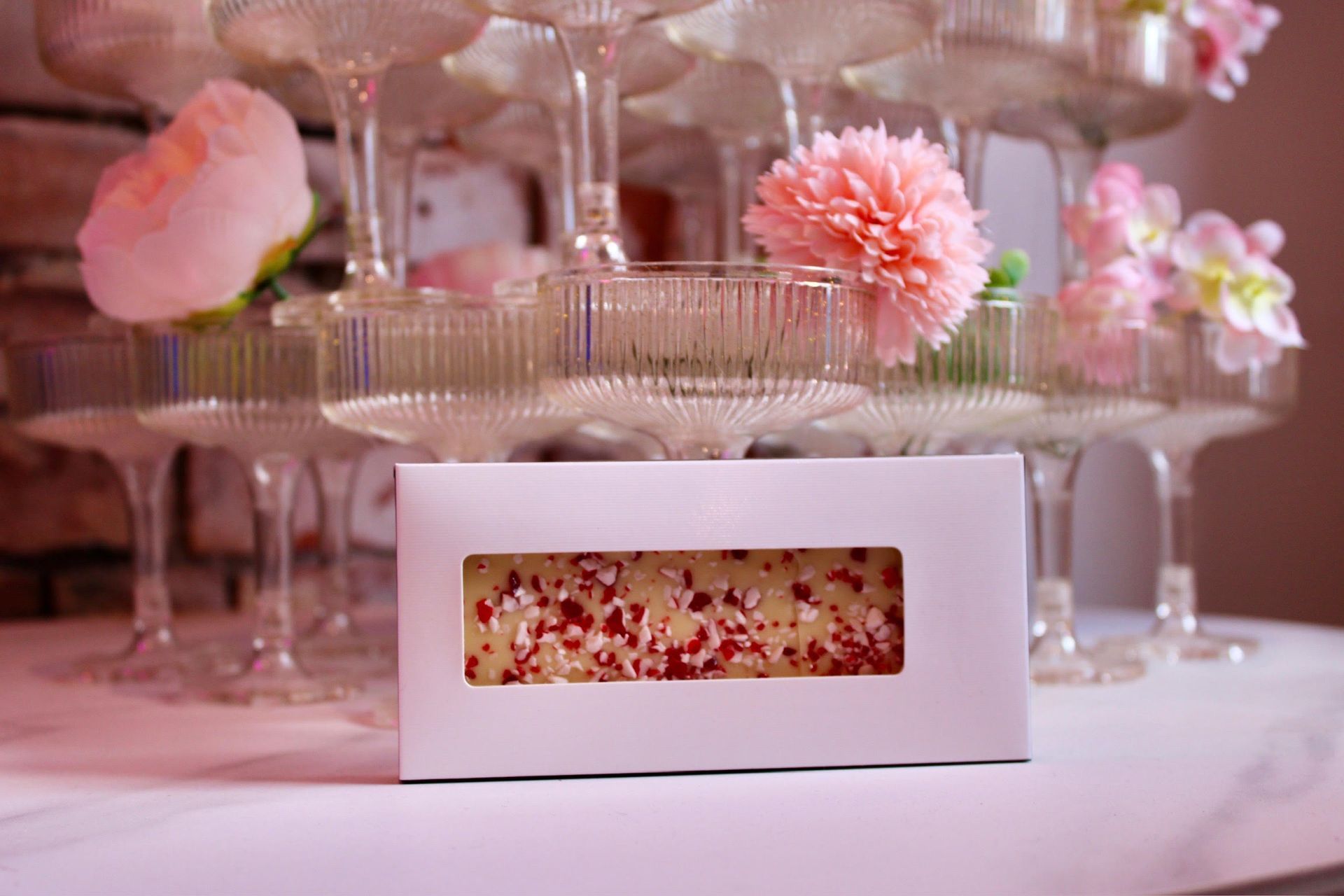 White box with window displaying candy bar, in front of champagne tower with pink flowers.