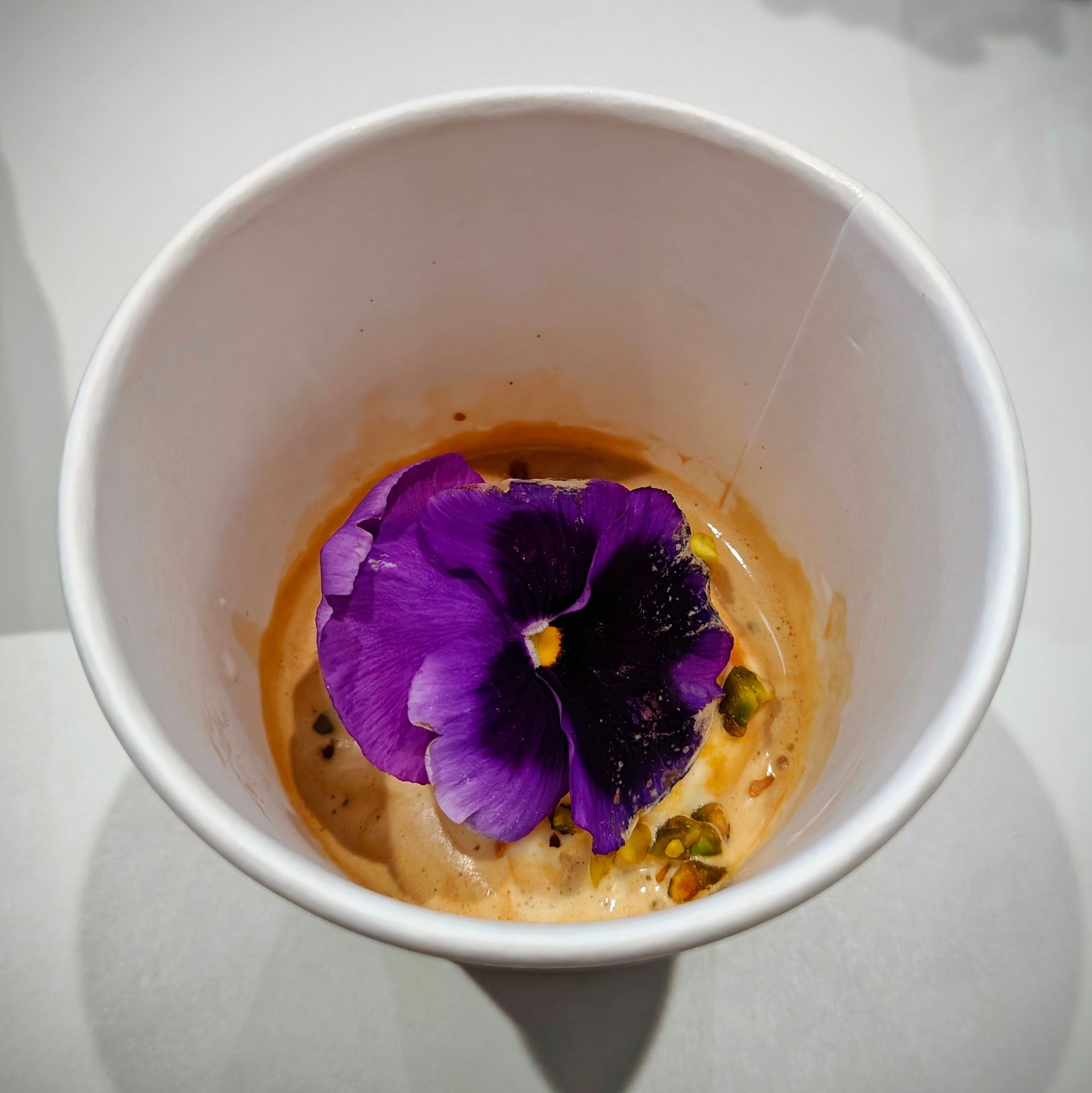 A cup of ice cream, topped with a purple flower and pistachio nuts.