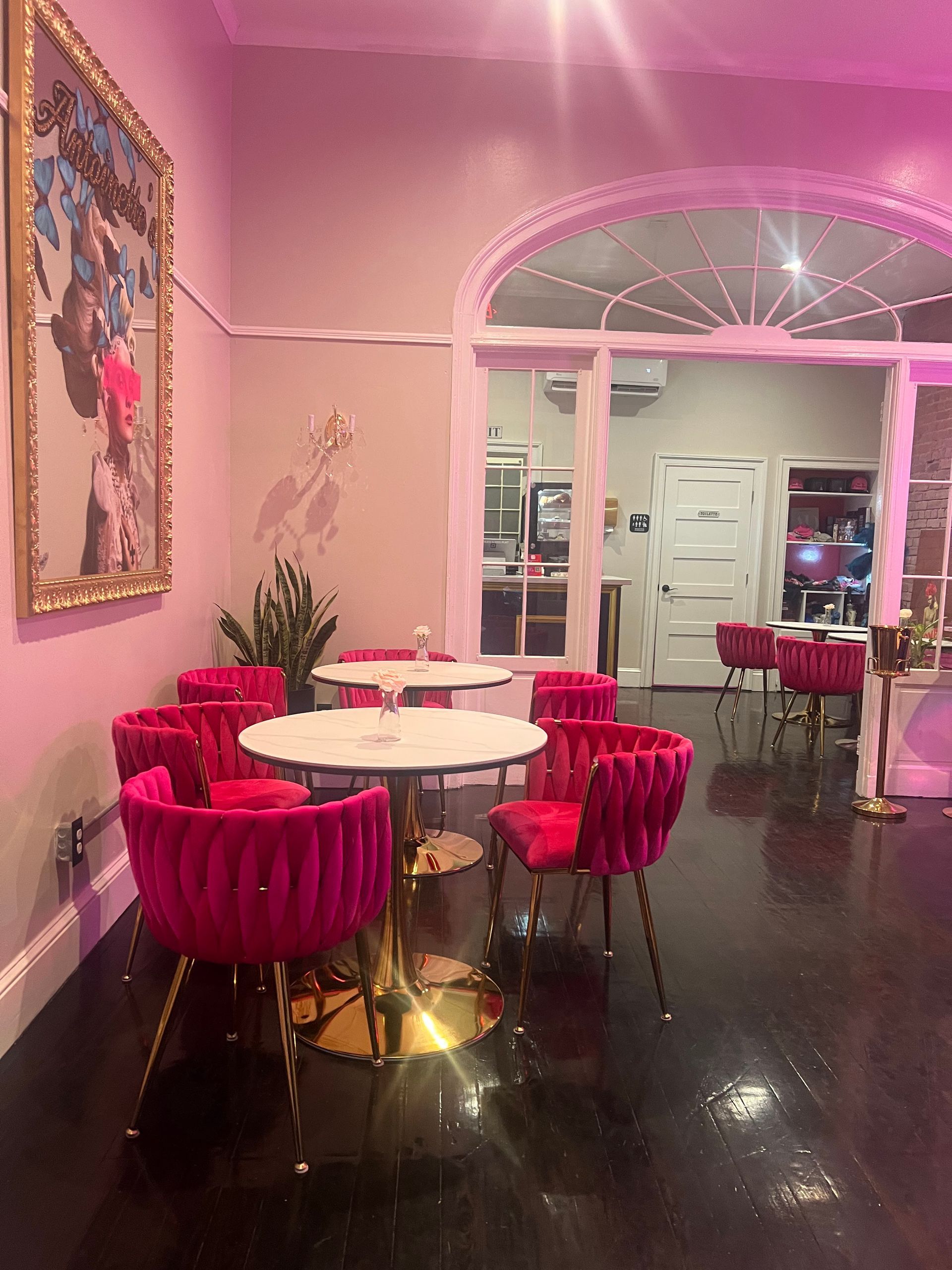 Pink-lit lounge area with velvet chairs, small tables, and a large mirror. A doorway leads to another room.
