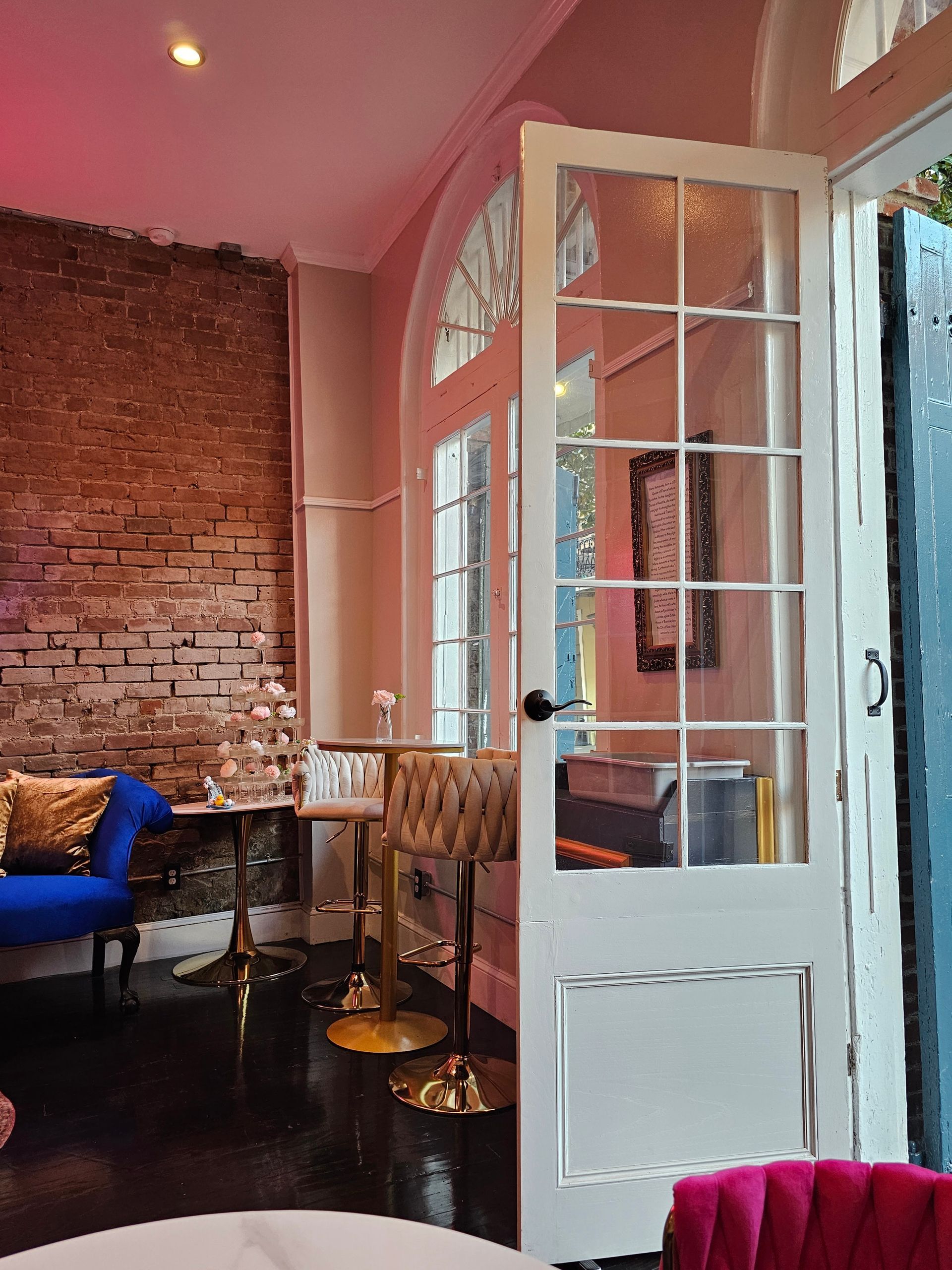 Interior with brick wall, blue couch, bar stools, and open glass door. Pink and gold decor.