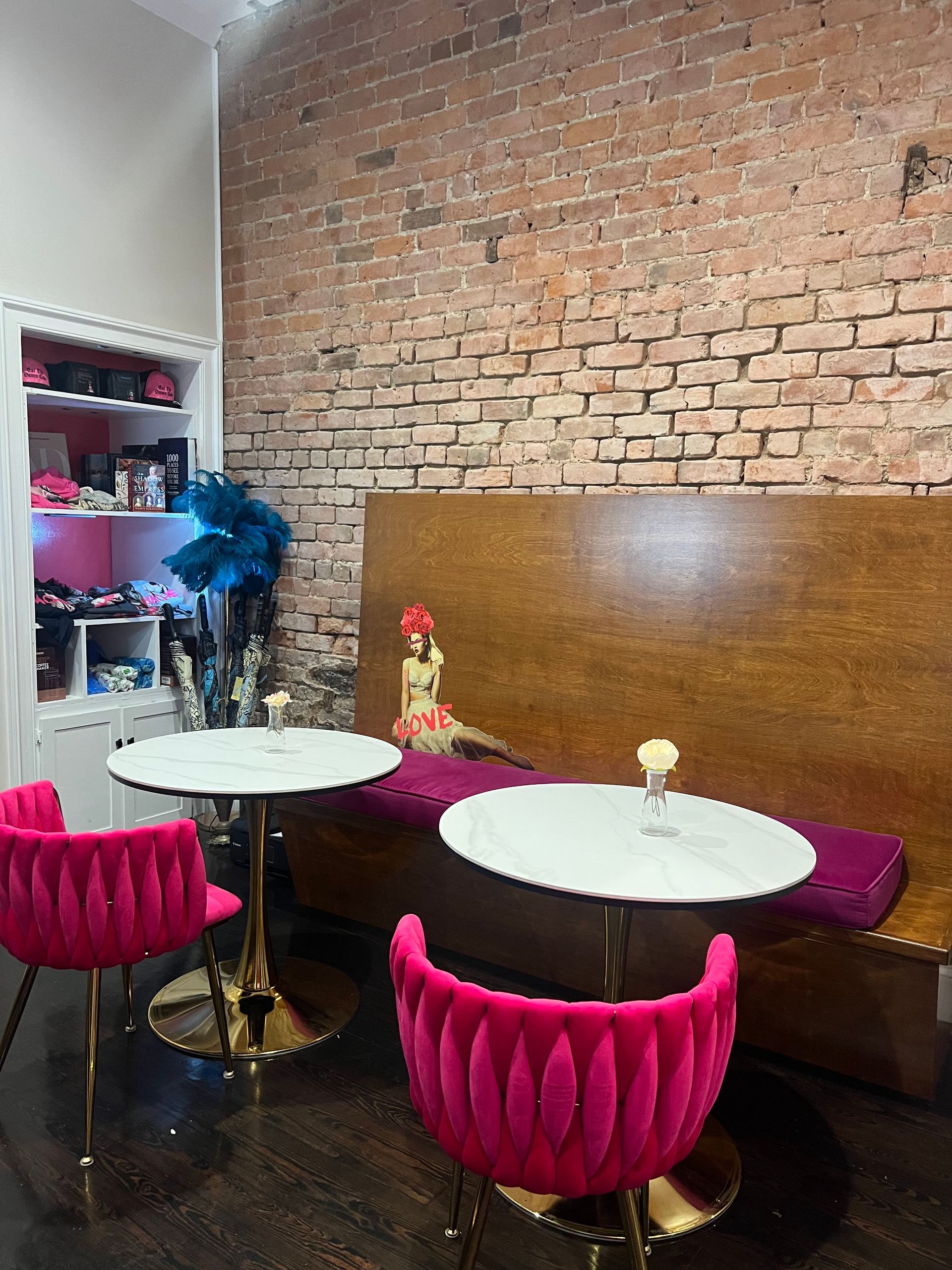 Interior with pink chairs, marble tables, and brick wall. Wooden booth seating.