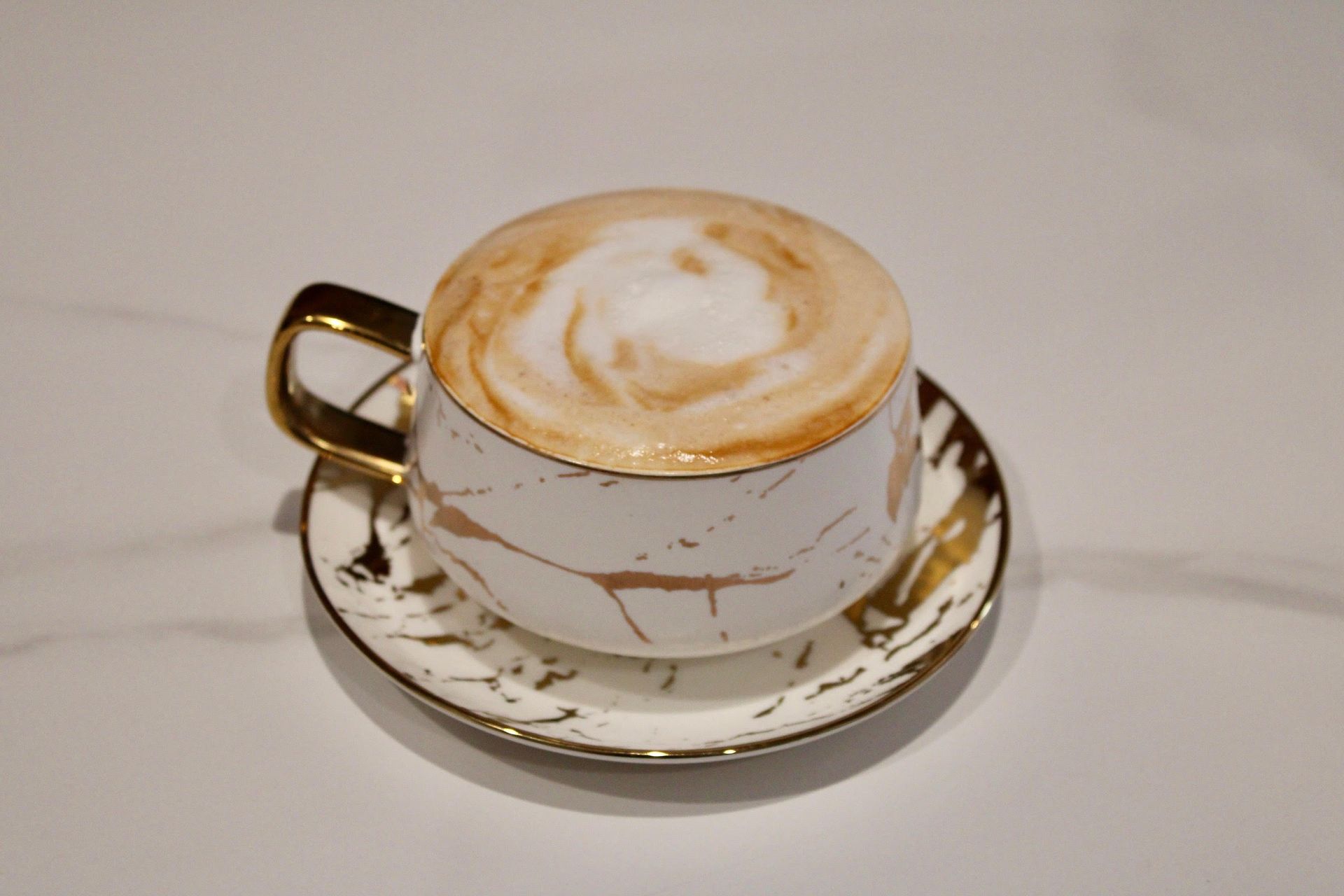 Cappuccino in a marble-patterned teacup with gold trim, resting on a matching saucer.