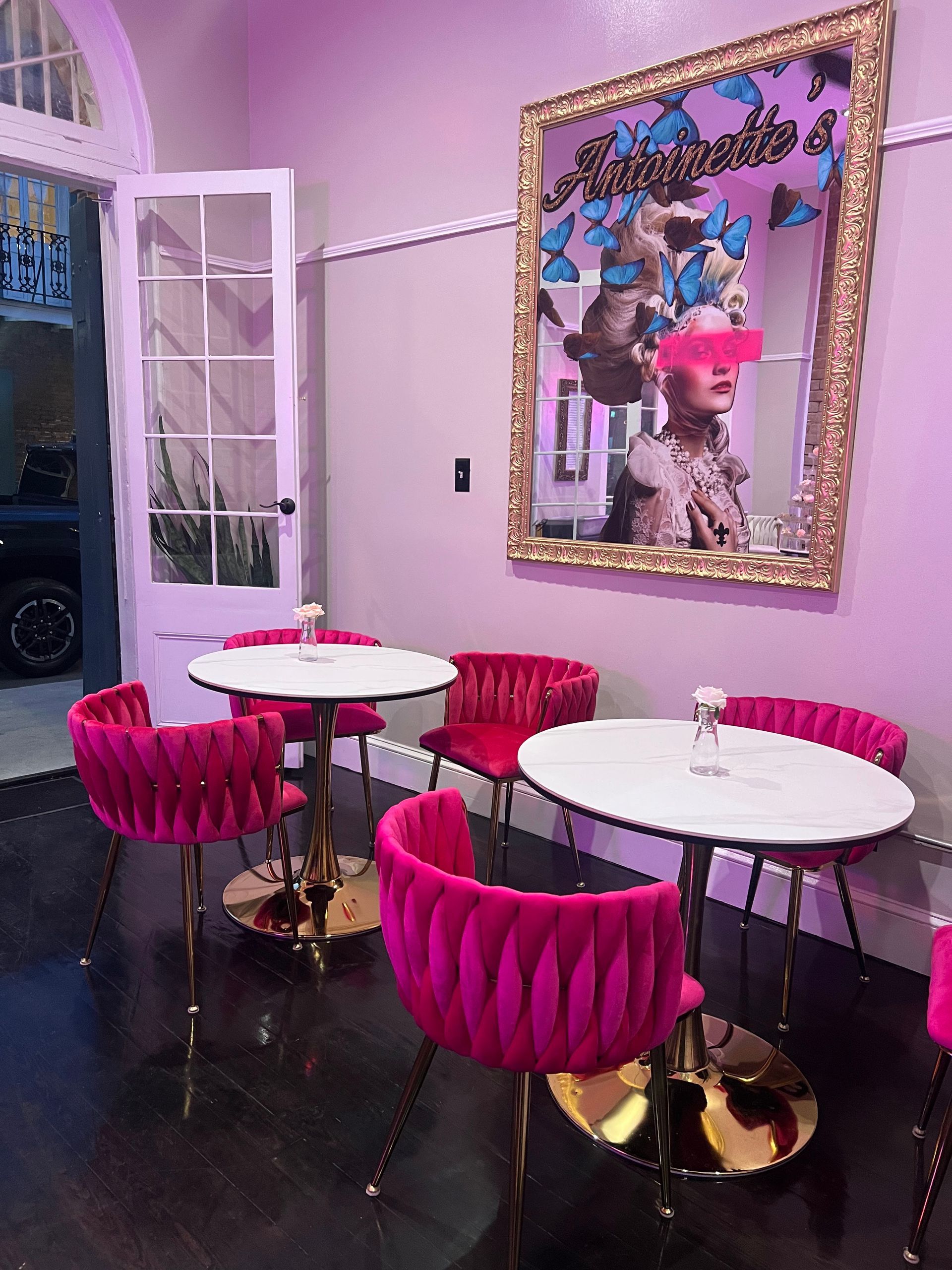Cafe seating area with pink velvet chairs, round tables, and a mirror with artwork.
