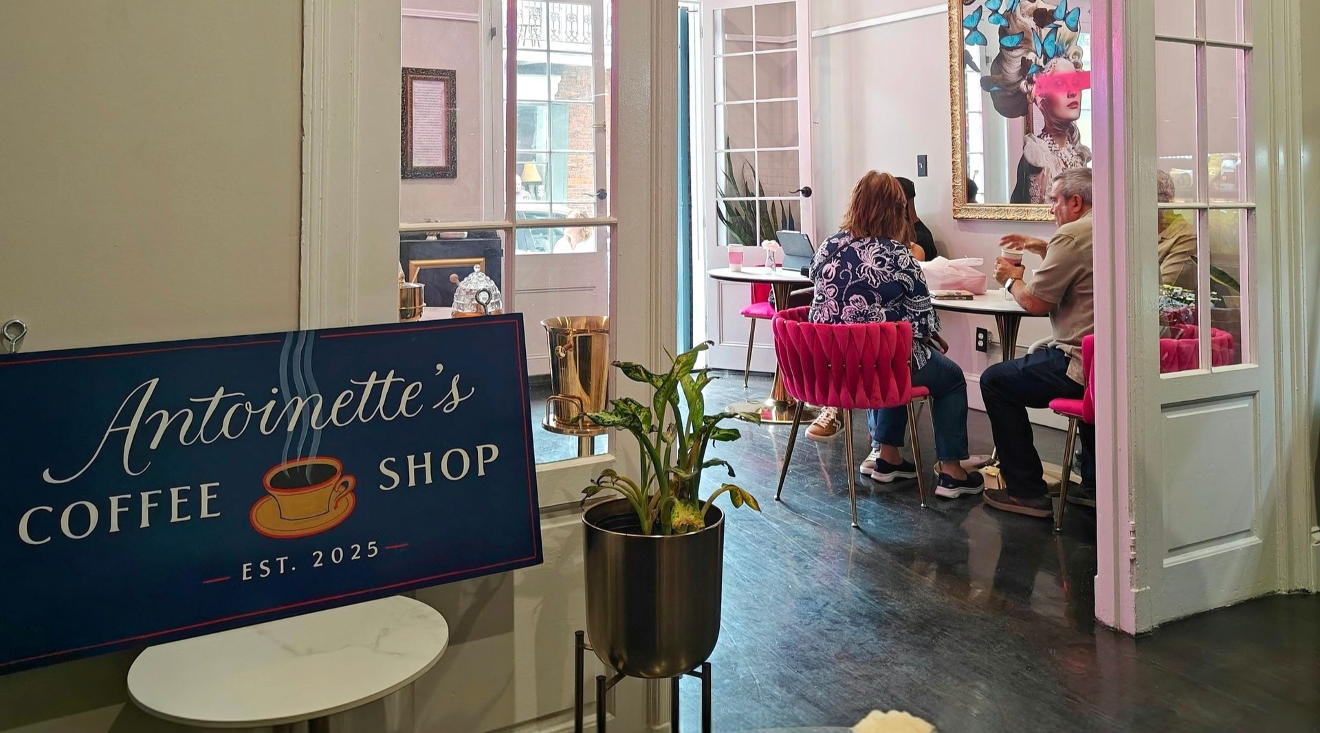 Antoinette's Coffee Shop: People seated at a table, coffee sign. Bright interior with a plant and decor.