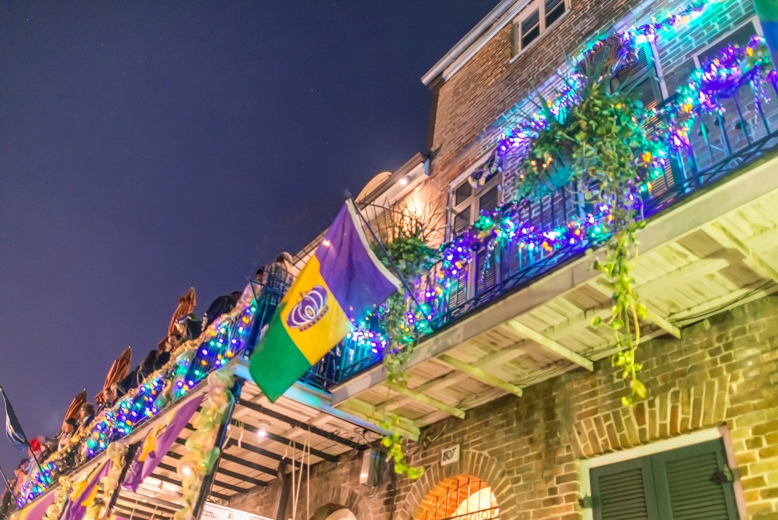 A balcony decorated with mardi gras lights and a flag.