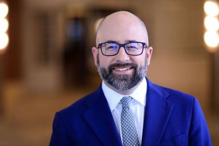 A man with a beard and glasses is wearing a suit and tie.