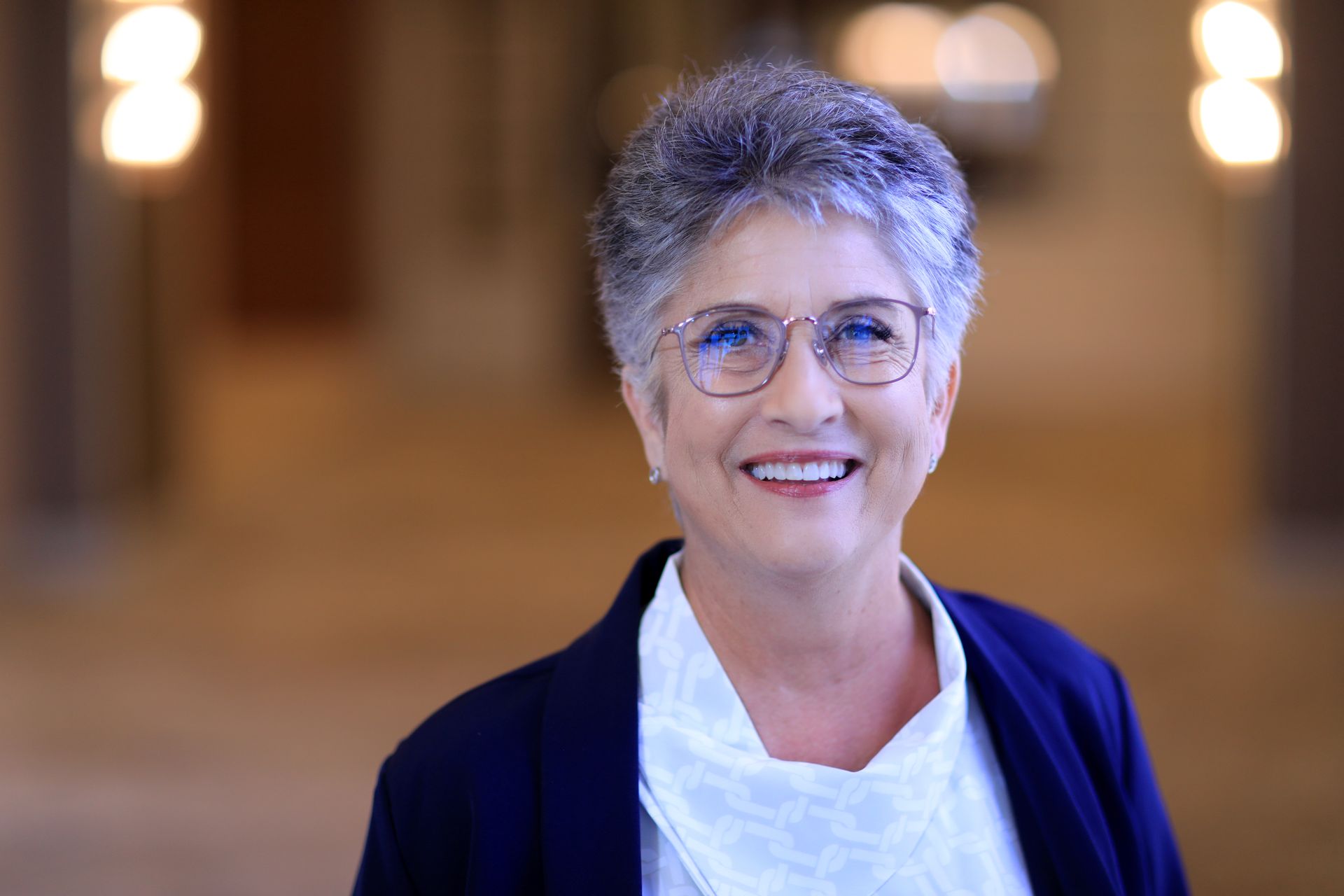 A woman wearing glasses and earrings is smiling for the camera.