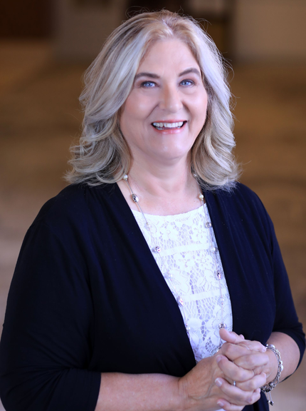 A woman in a blue jacket and white shirt is smiling for the camera.