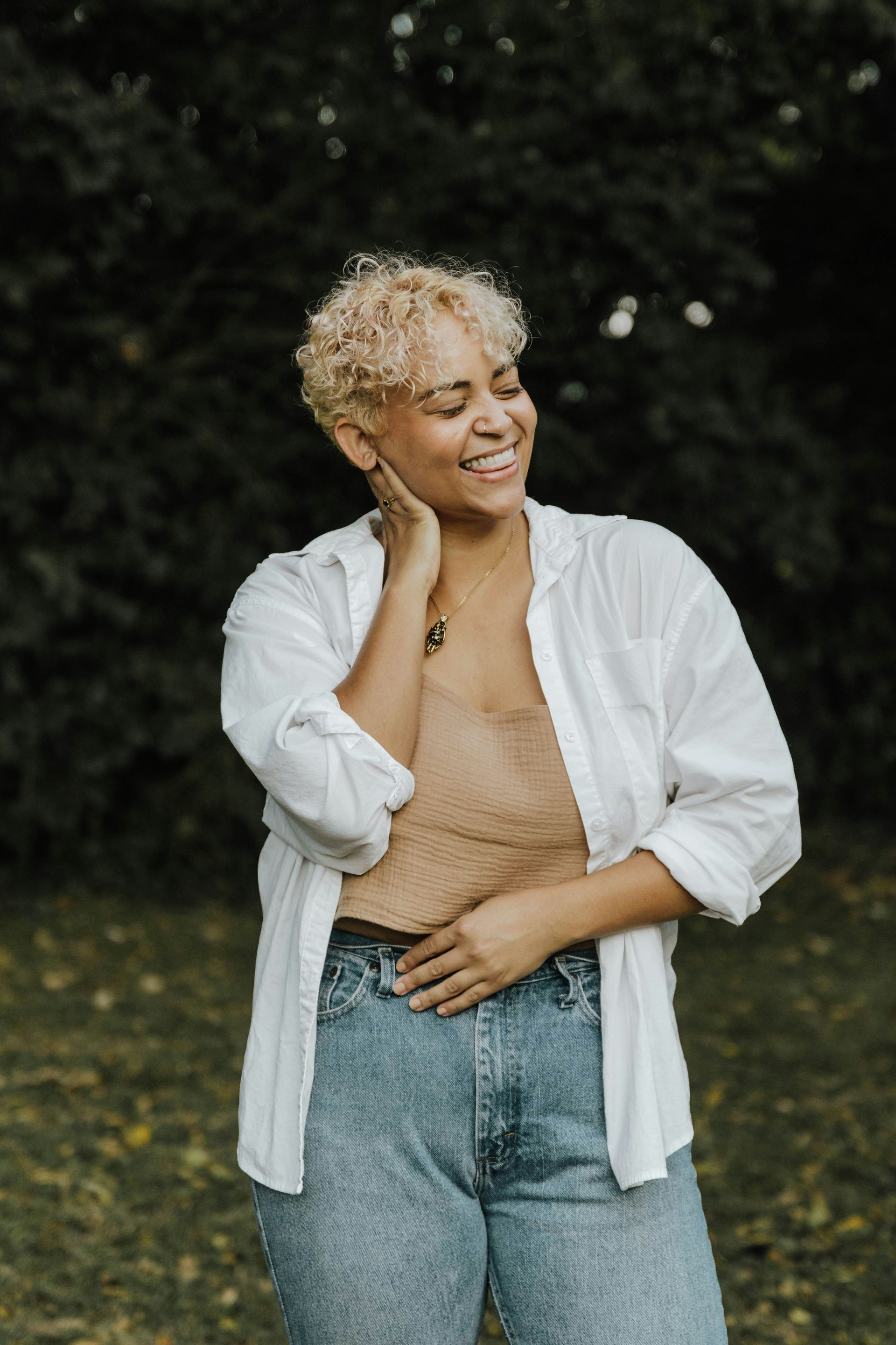 A woman wearing a white shirt and jeans is standing in a park.