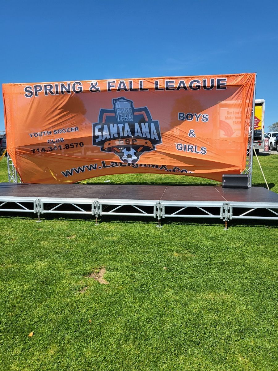 A large orange banner is sitting on top of a stage in a grassy field.