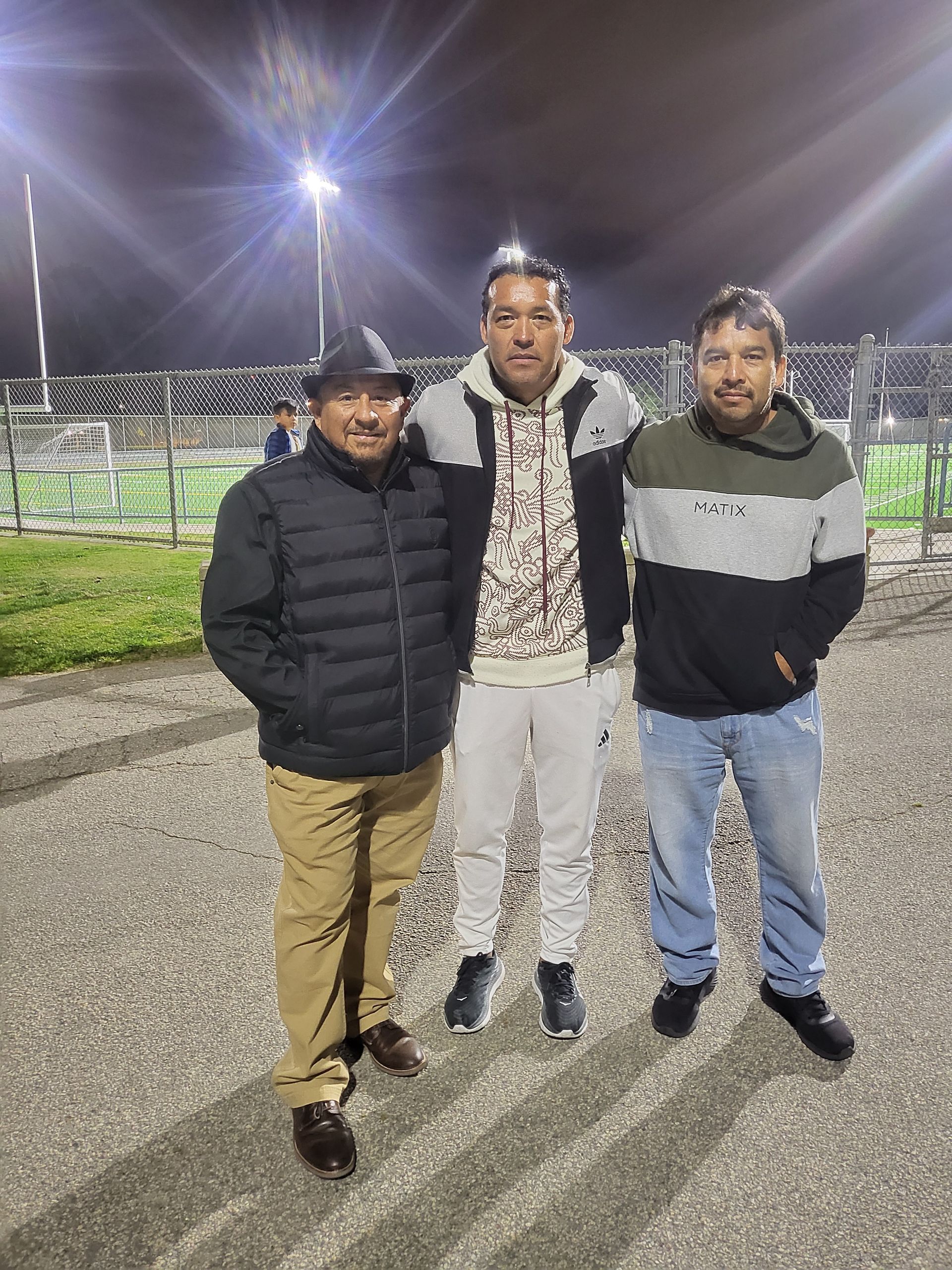 Three men are standing next to each other in a parking lot at night  - Santa Ana, CA - Mesa Verde Youth Soccer League 