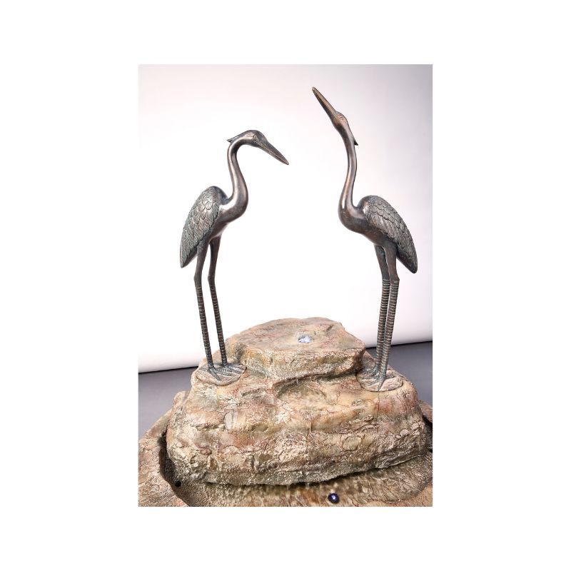Bronze heron sculptures on a rock formation. One looks up, the other looks forward.