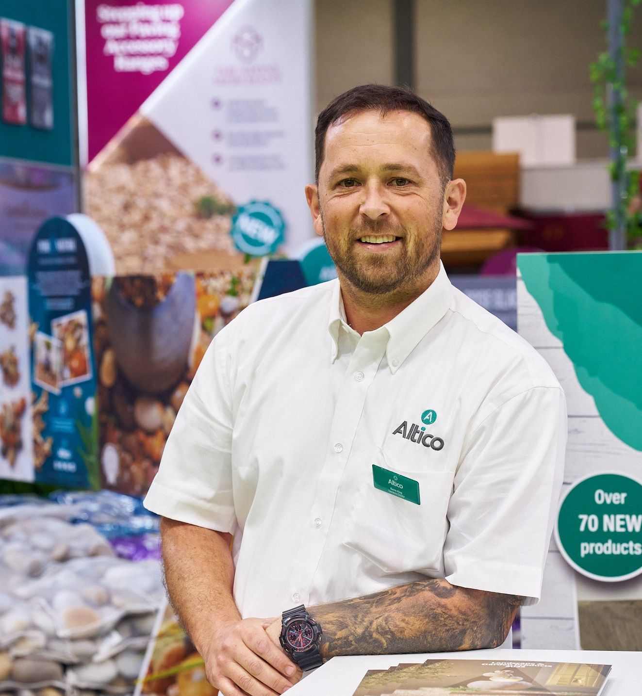 Man in white shirt with company logo, smiling at a trade show booth, surrounded by products.
