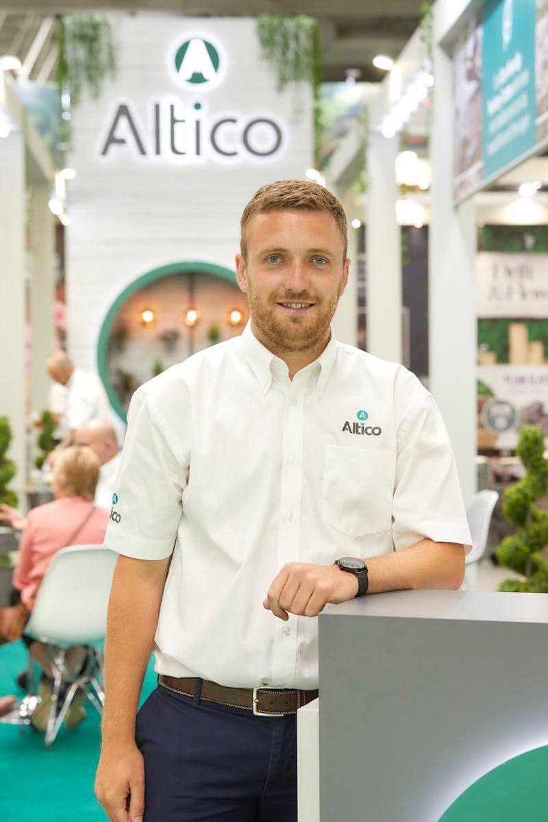 Man in white shirt with company logo stands at a booth.