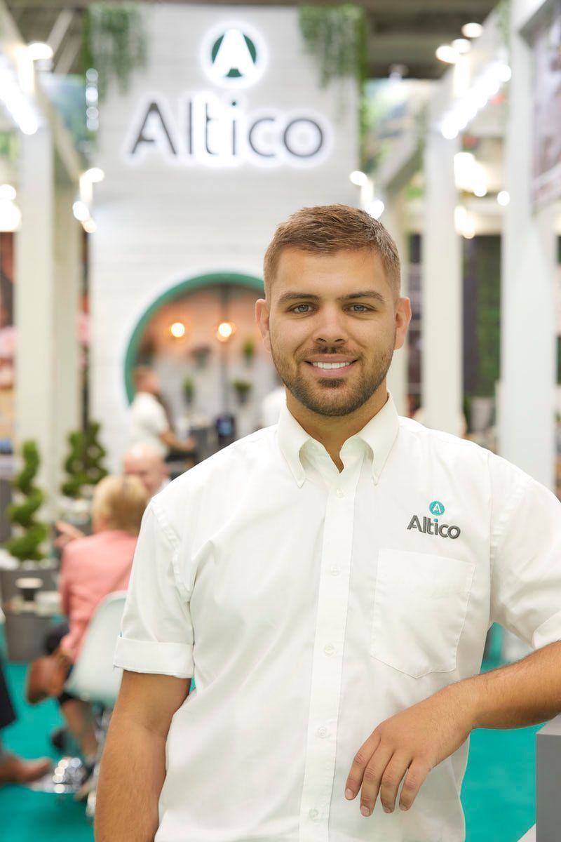 Man in a white shirt with Altico logo smiles in front of an Altico booth.