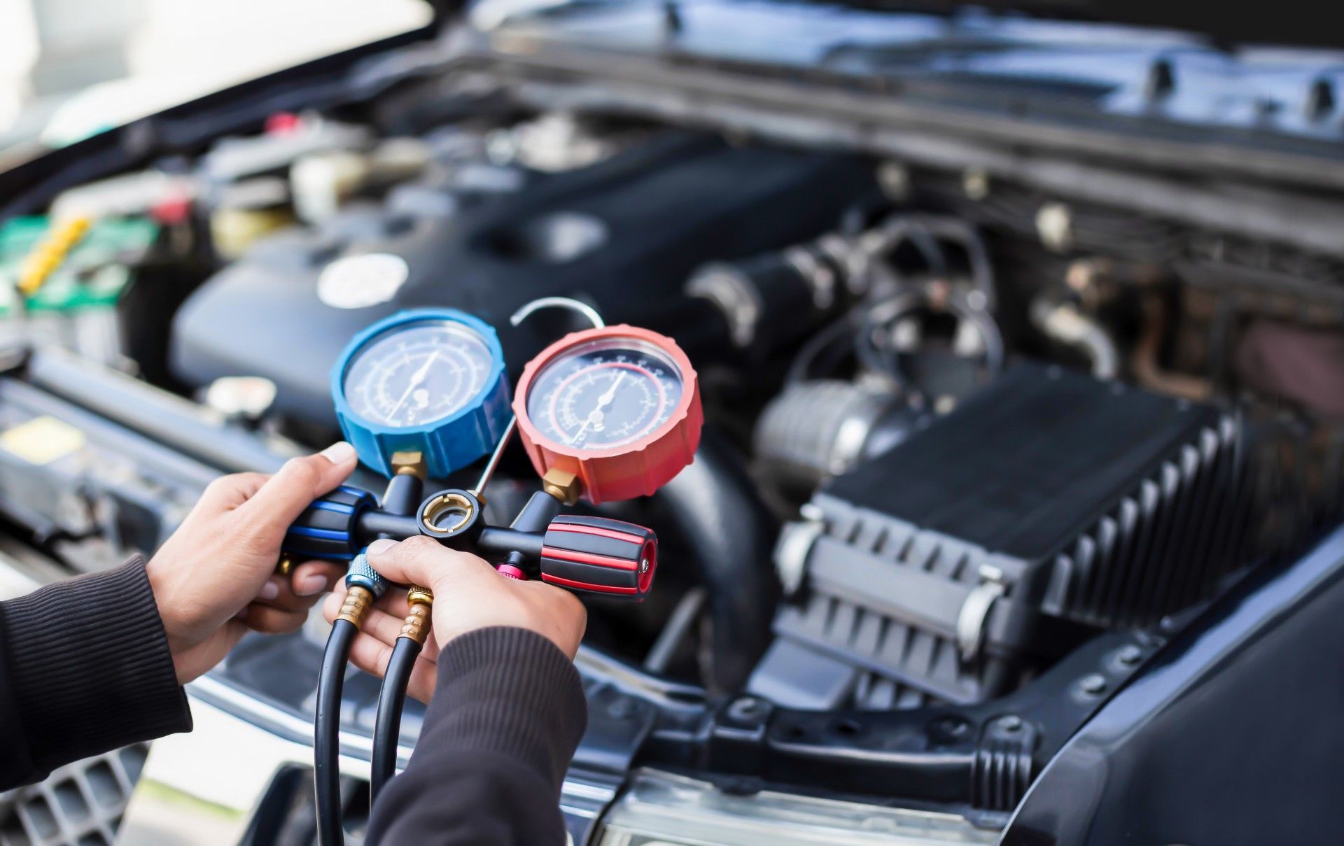 A person is holding a gauge in front of a car engine.