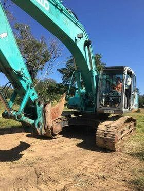 A Green Excavator Is Sitting On Top Of A Dirt Field — GCE Earthworks Pty Ltd In Krambach, NSW
