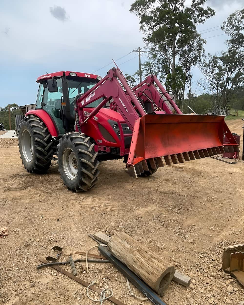 A Red Tractor With A Bulldozer Attached To It Is Parked In A Dirt Field — GCE Earthworks Pty Ltd In Krambach, NSW
