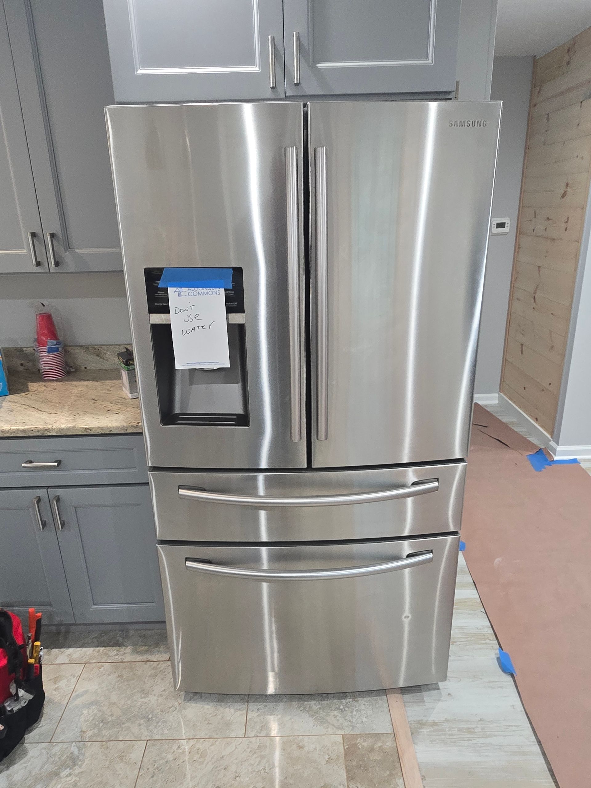 Stainless steel refrigerator in a kitchen with gray cabinets and granite countertop.