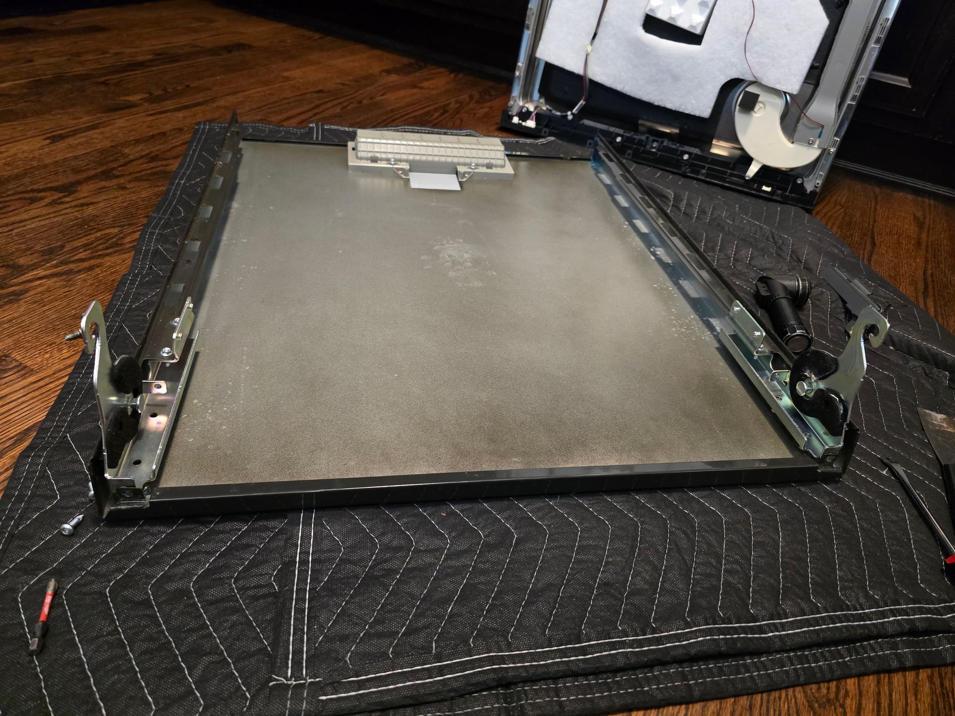 Disassembled computer monitor on a black mat, showing the screen panel and detached frame components.
