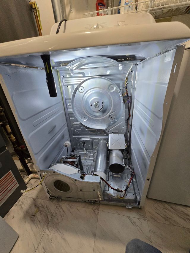 Open white dryer, interior components exposed. Silver drum and vent, wires, and a flashlight.