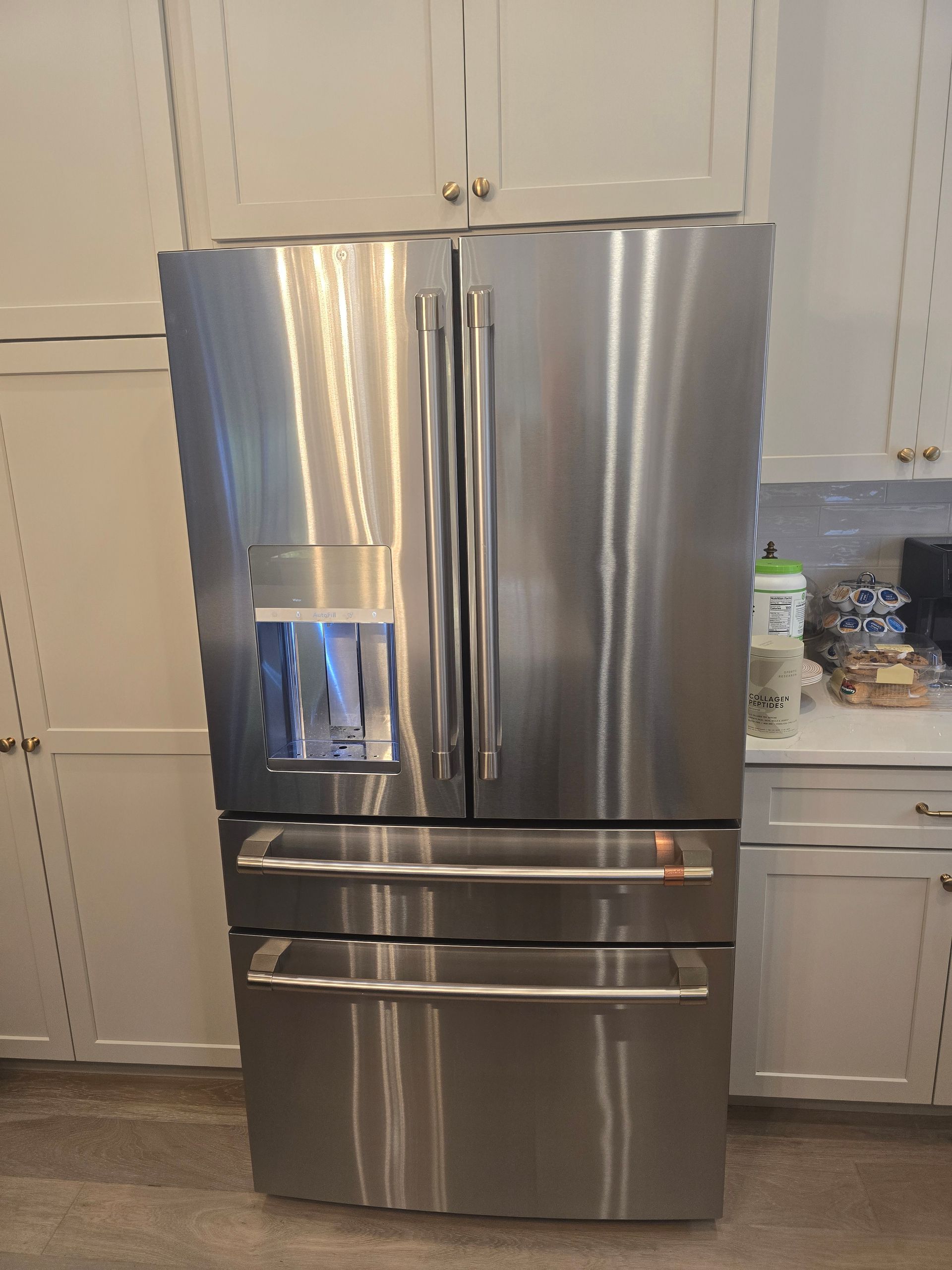Stainless steel French door refrigerator in a kitchen with white cabinets.