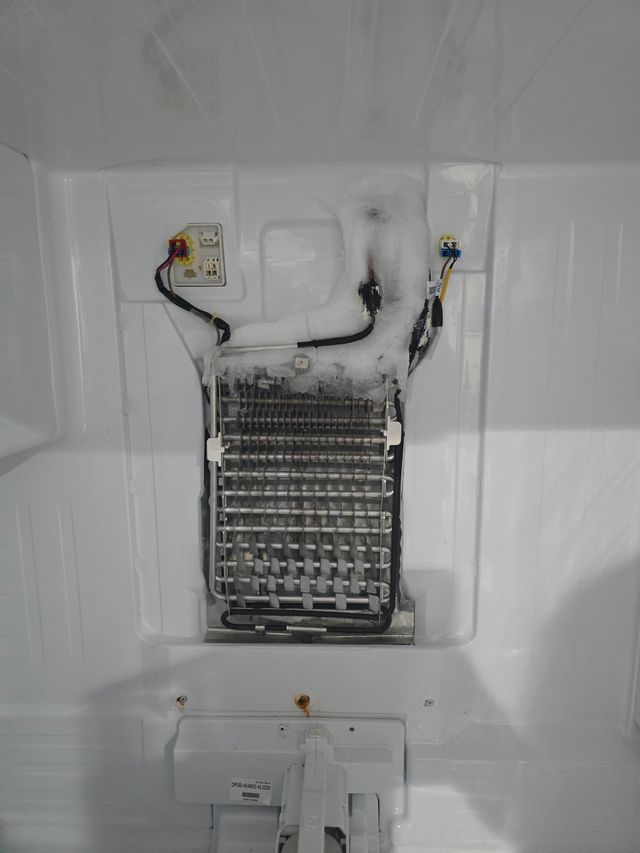 Inside a white refrigerator: a heavily frosted evaporator coil.