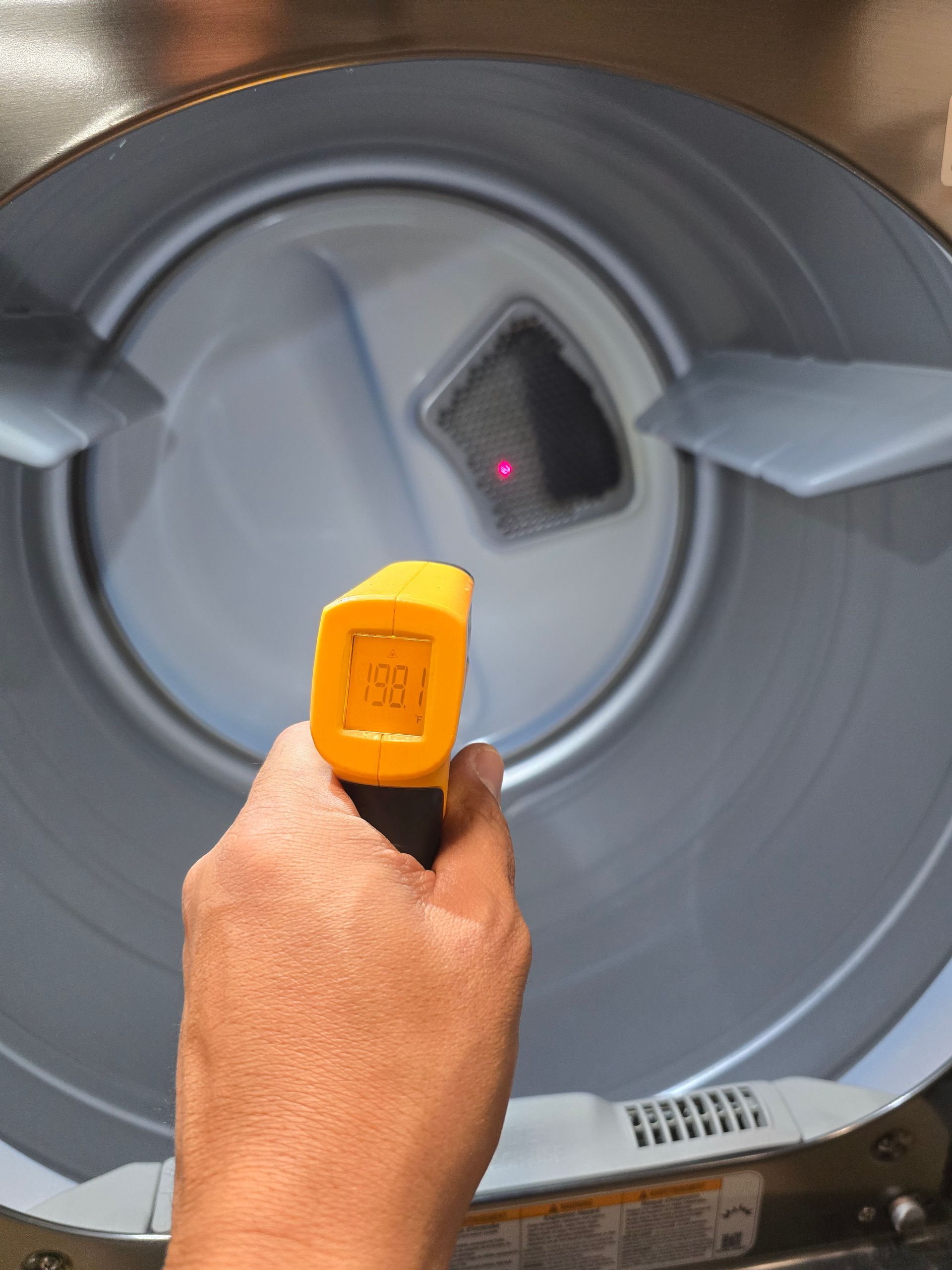 Hand holding a yellow infrared thermometer inside a dryer, with the temperature reading 88.