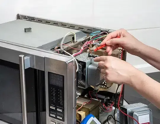 Person testing the electrical components of an open microwave with a multimeter.