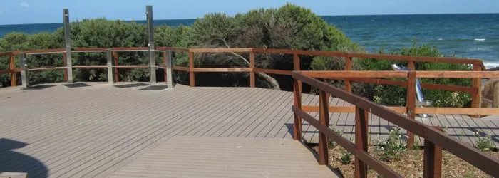 A Wooden Walkway Leading To The Ocean With A Wooden Railing — Johnson's Timber Agencies In Ulladulla, NSW