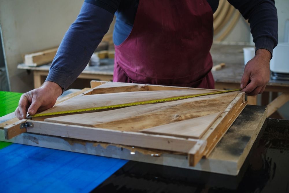 A Man Is Measuring A Piece Of Wood With A Tape Measure — Johnson's Timber Agencies In Ulladulla, NSW