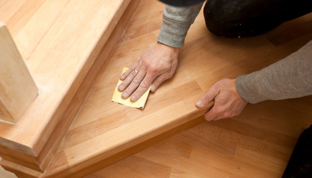 A Person Is Sanding A Wooden Staircase With A Sandpaper — Johnson's Timber Agencies In Ulladulla, NSW