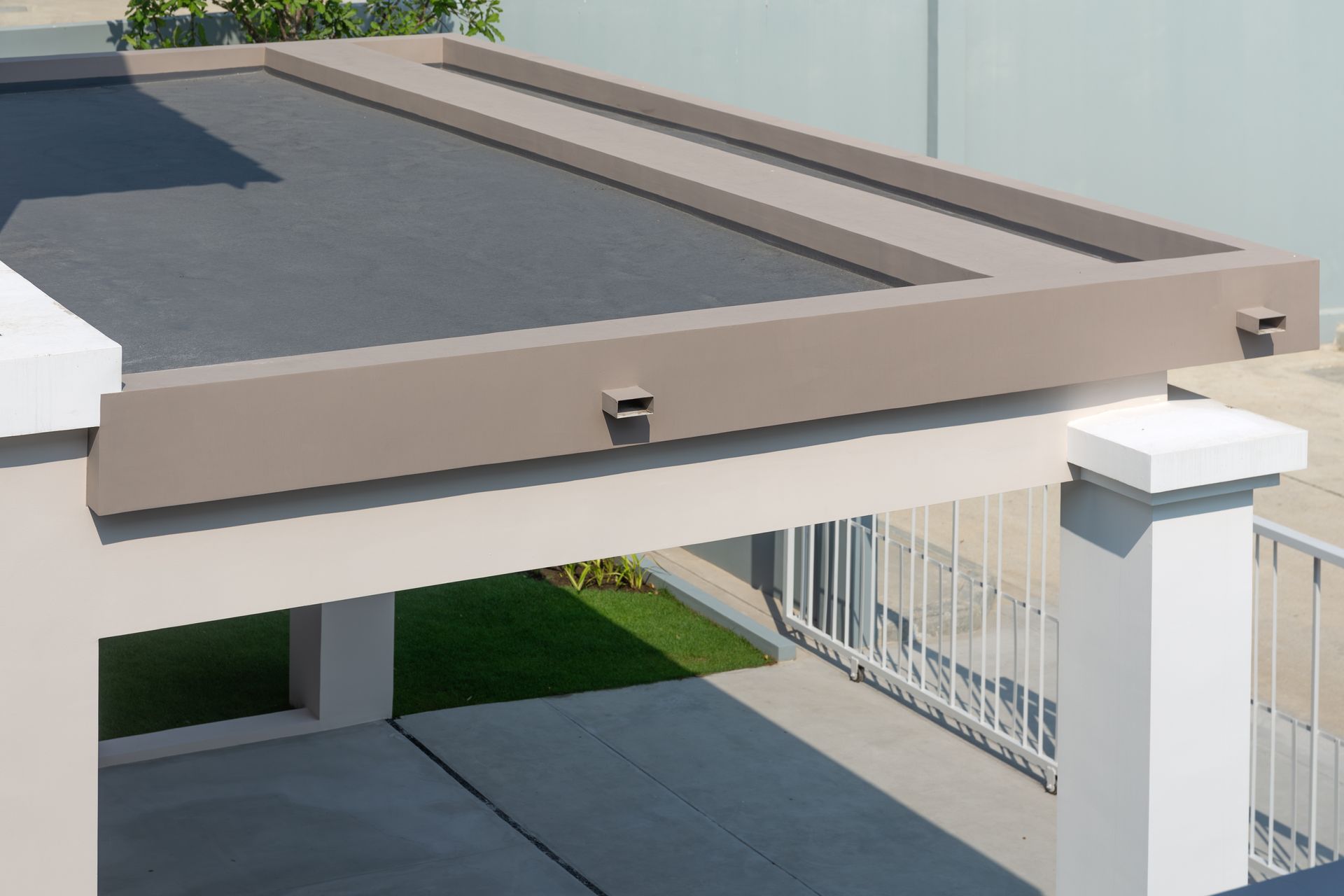 Modern patio pergola with beige frame, dark roof panels, and white support posts beside a driveway
