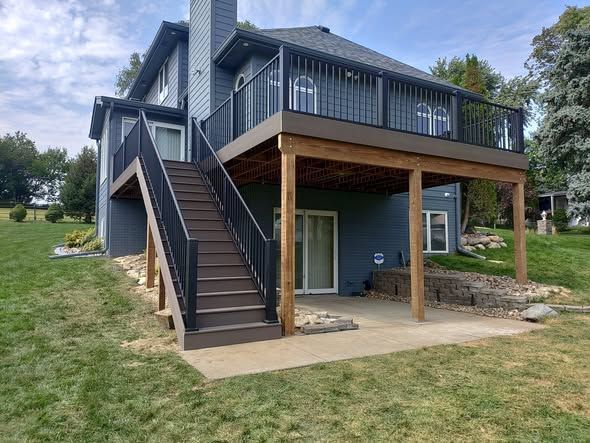 Two-story house with dark blue siding and a brown deck, stairs, and railing.
